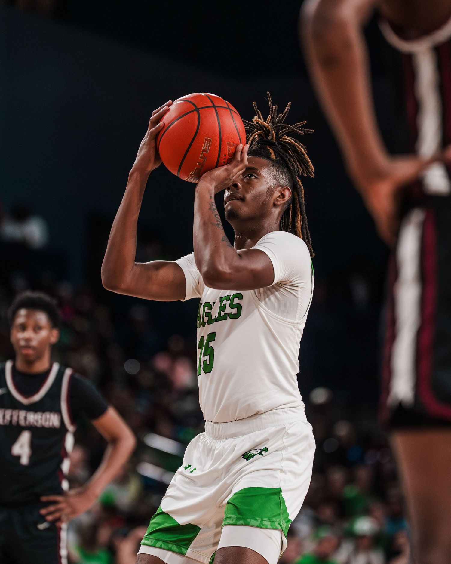 Basketball player #5 in green Eagles uniform shoots during a competitive game against Jefferson team.