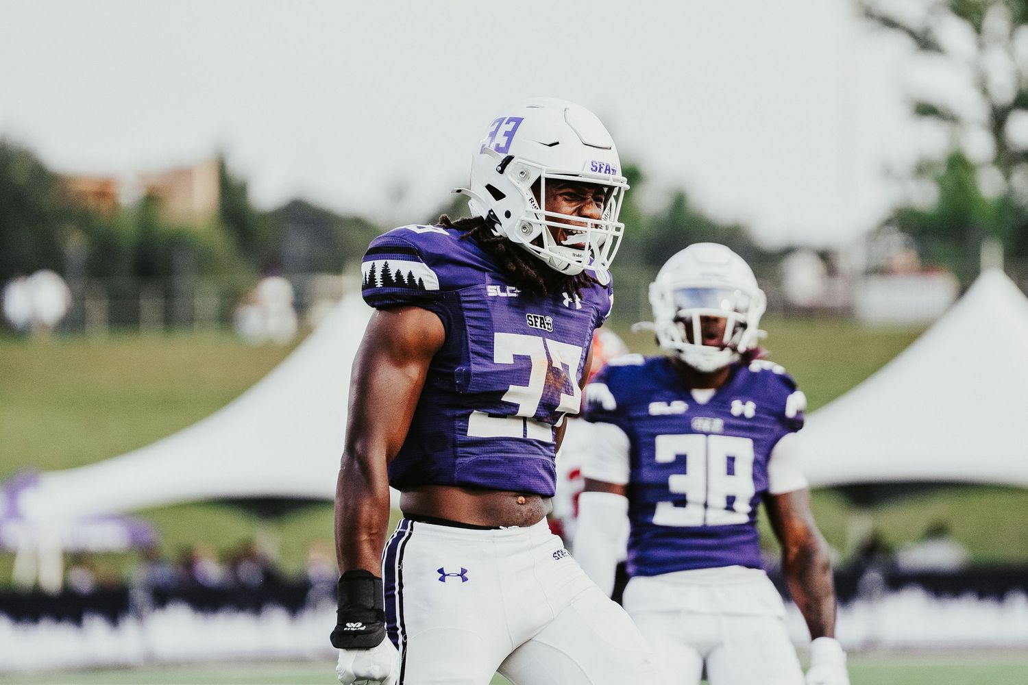 Football players in purple and white uniforms run drills during an outdoor practice session.