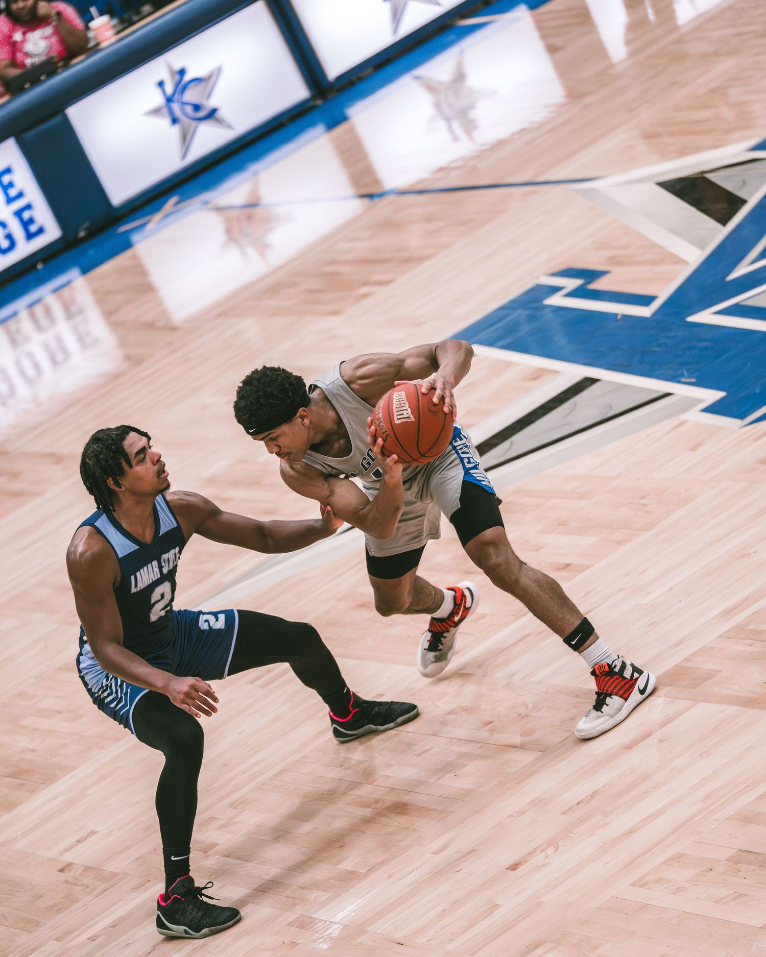 Two basketball players compete for the ball during an intense college game on a hardwood court.