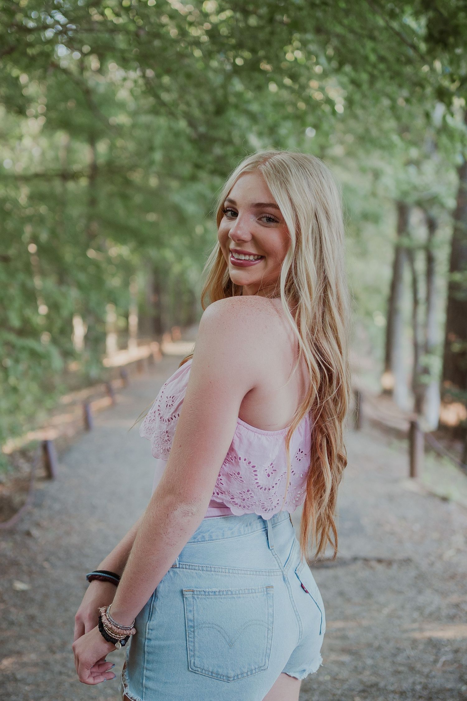 Person in pink top and denim shorts poses on forest trail.