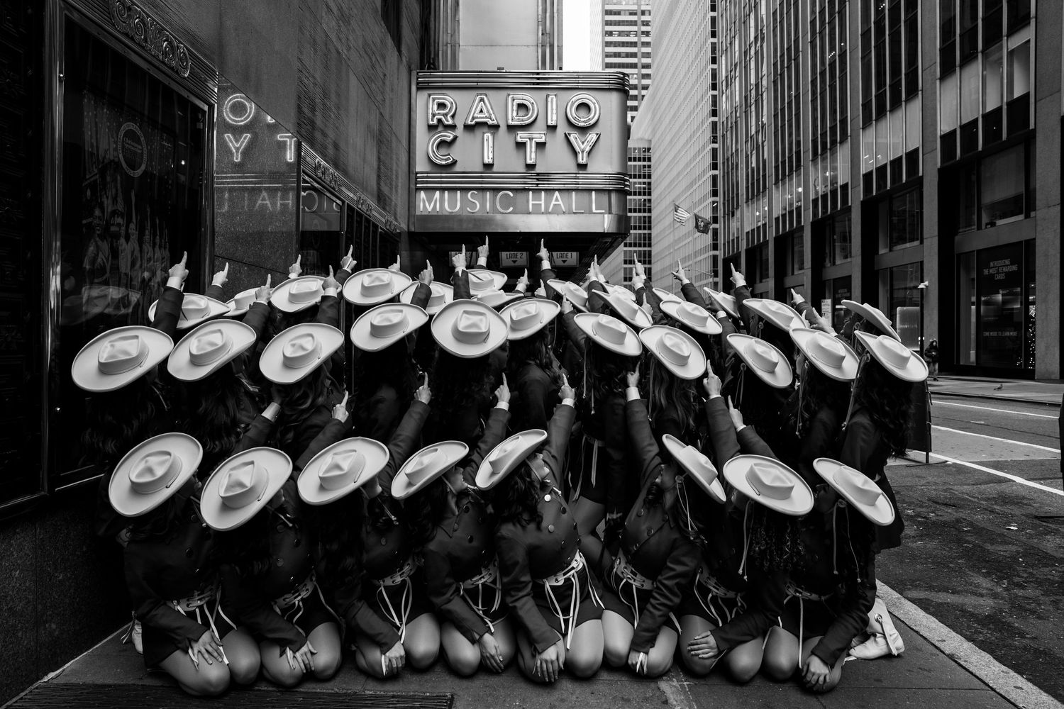 Black and white photo of multiple cowboy hats hanging on a wall in a row at a western store.
