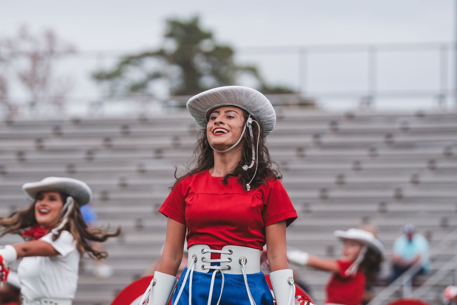 Performers in western-style costumes smiling during outdoor dance routine at stadium venue.