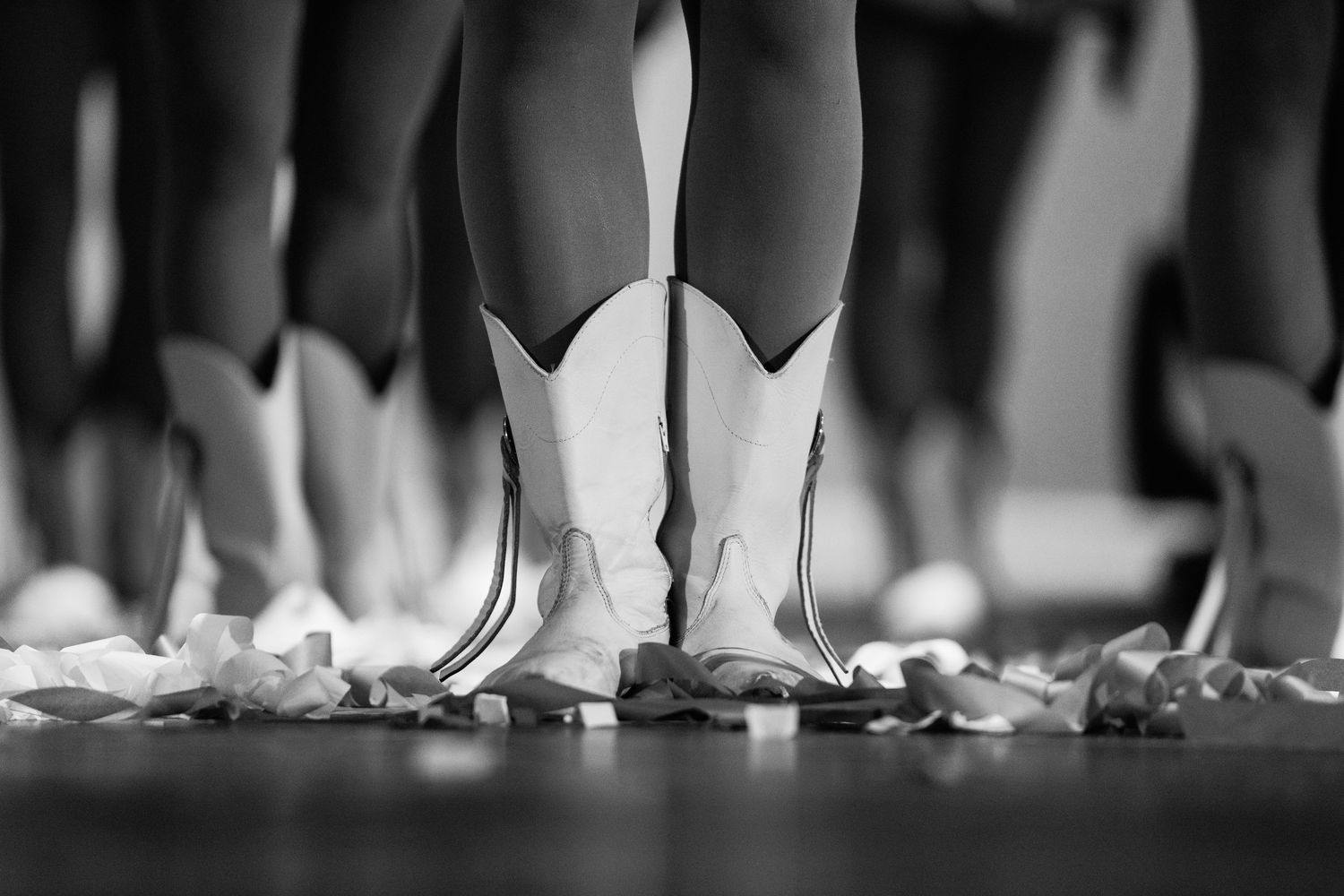 Black and white photo of ballet dancers in white pointe shoes standing on a stage scattered with rose petals.