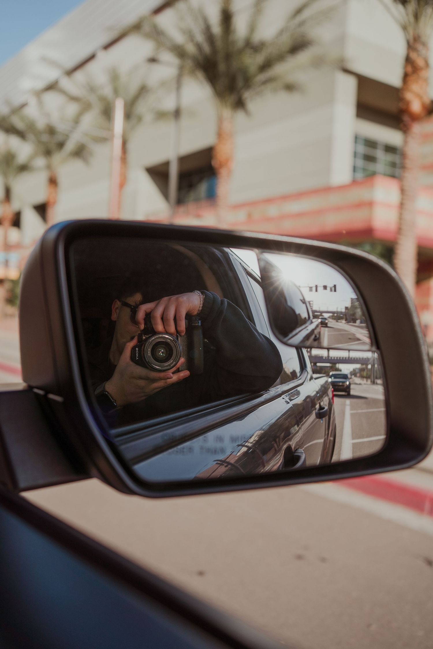 A sequence of car side mirror reflections showing a camera being held up against a palm tree backdrop in a parking lot.