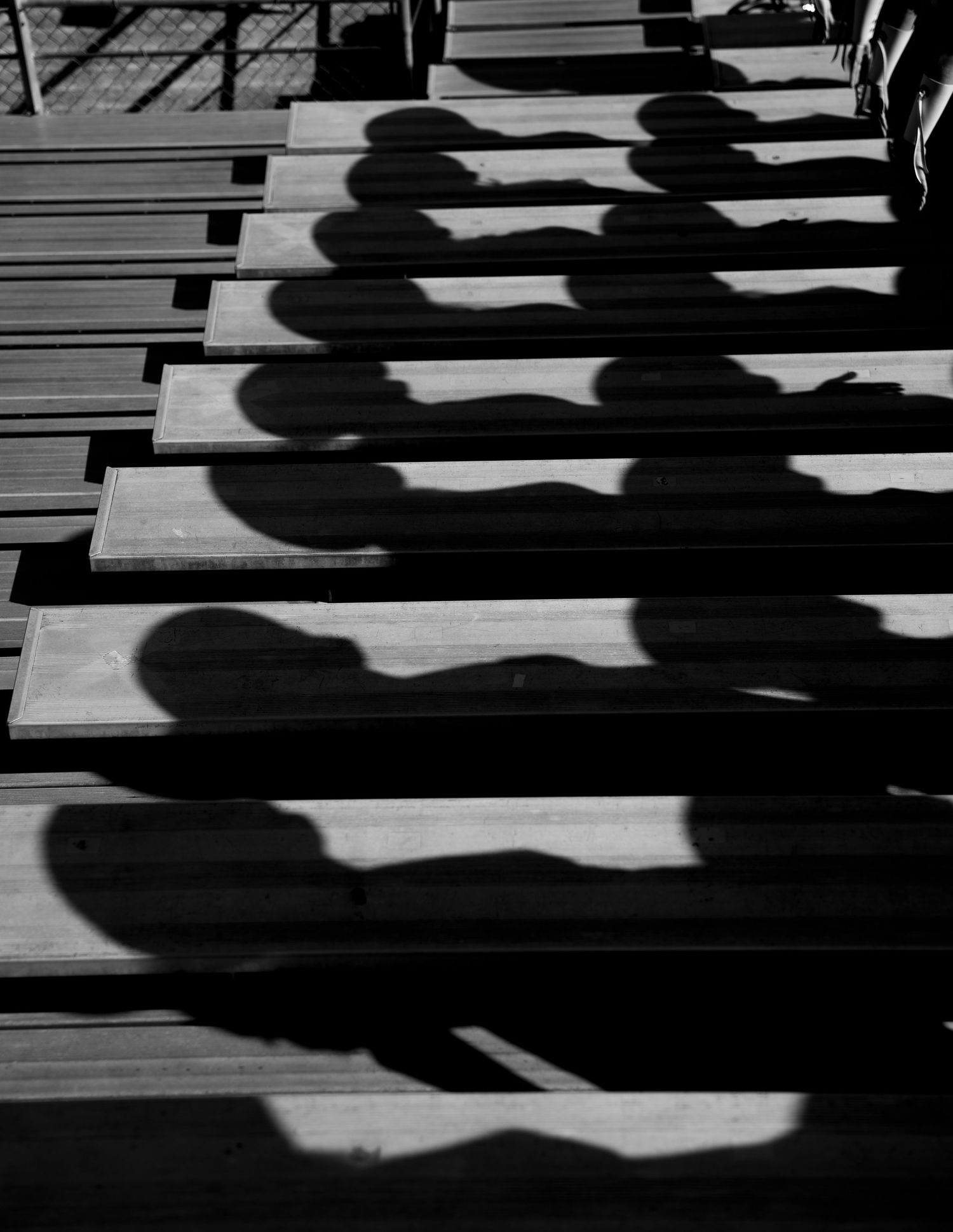 Dramatic shadows cast by people on wooden bleachers or steps create a striking black and white pattern.