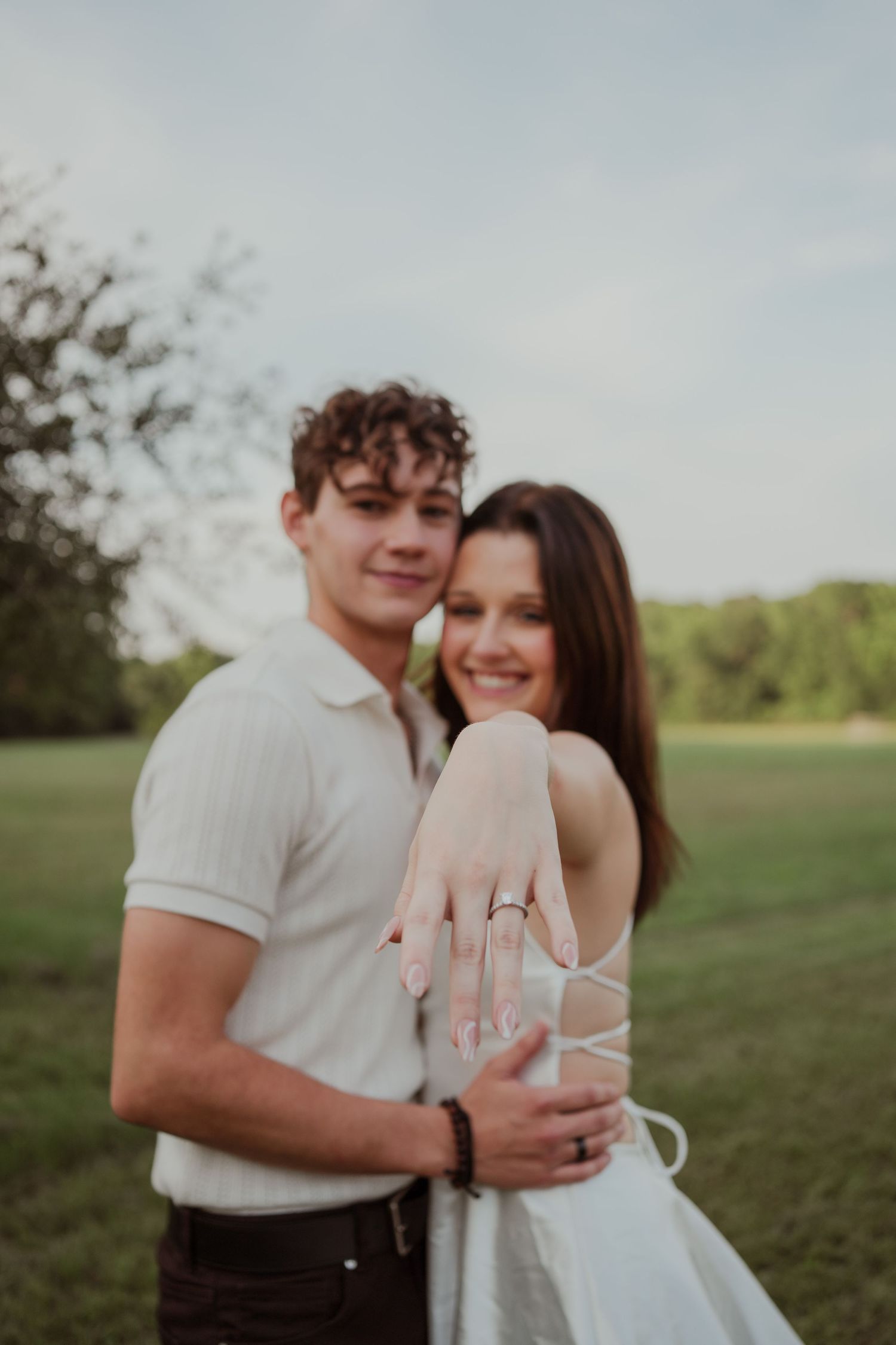 Engaged couple shows off ring during romantic outdoor photoshoot.
