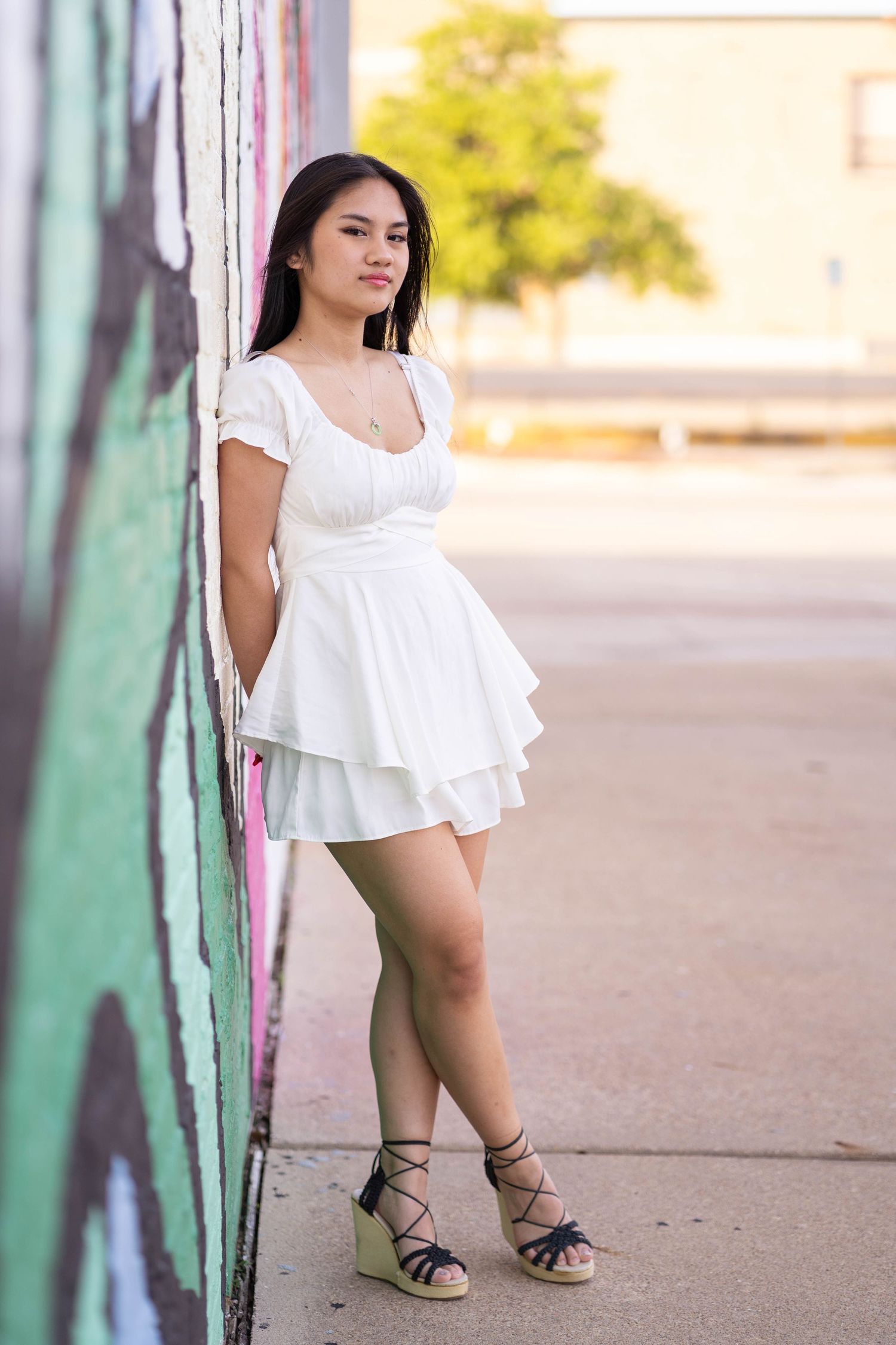 Person in white ruffle dress poses against colorful wall in urban setting.
