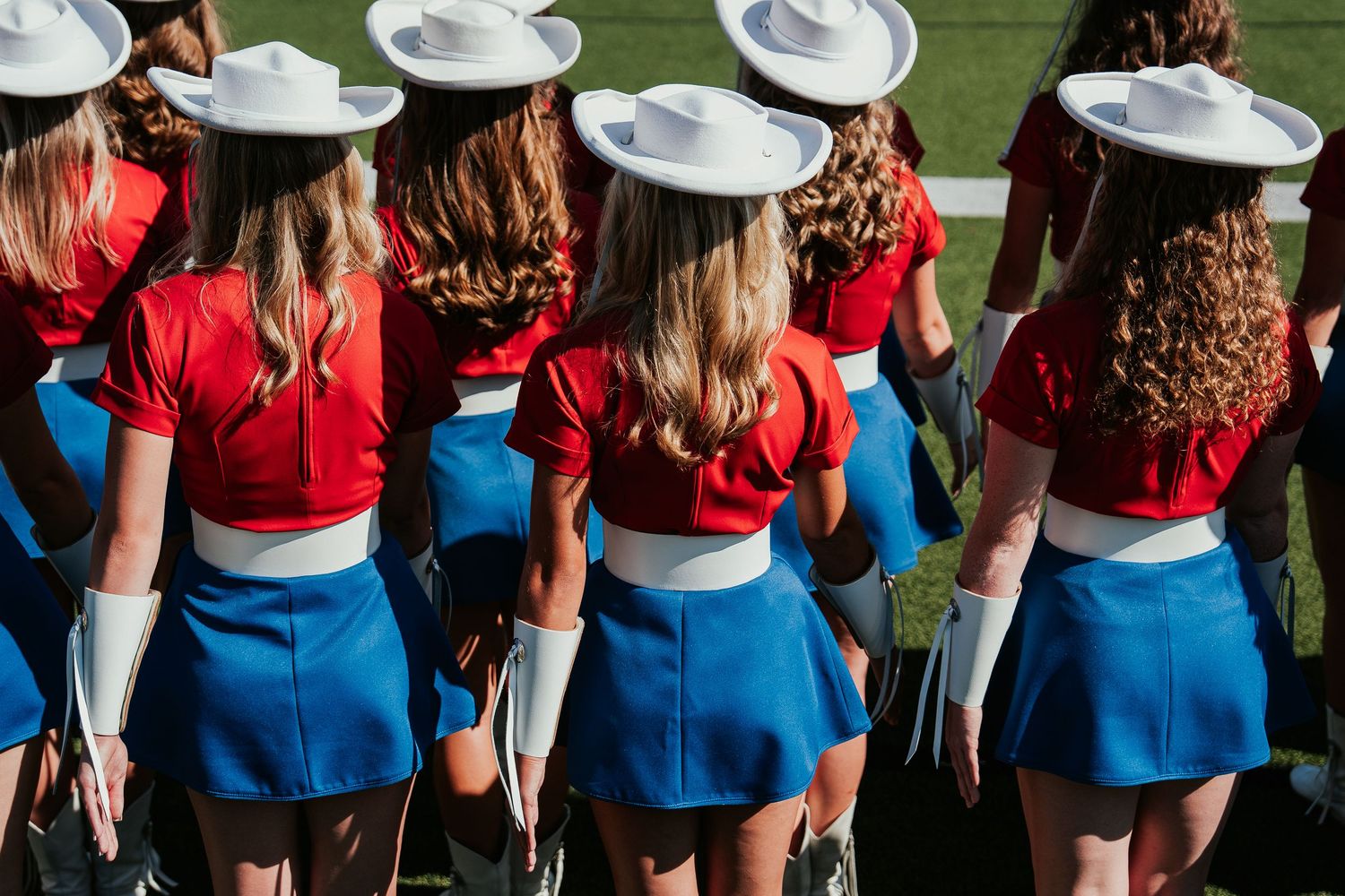 A row of cheerleaders in blue and red uniforms stand in formation on a field during a performance.