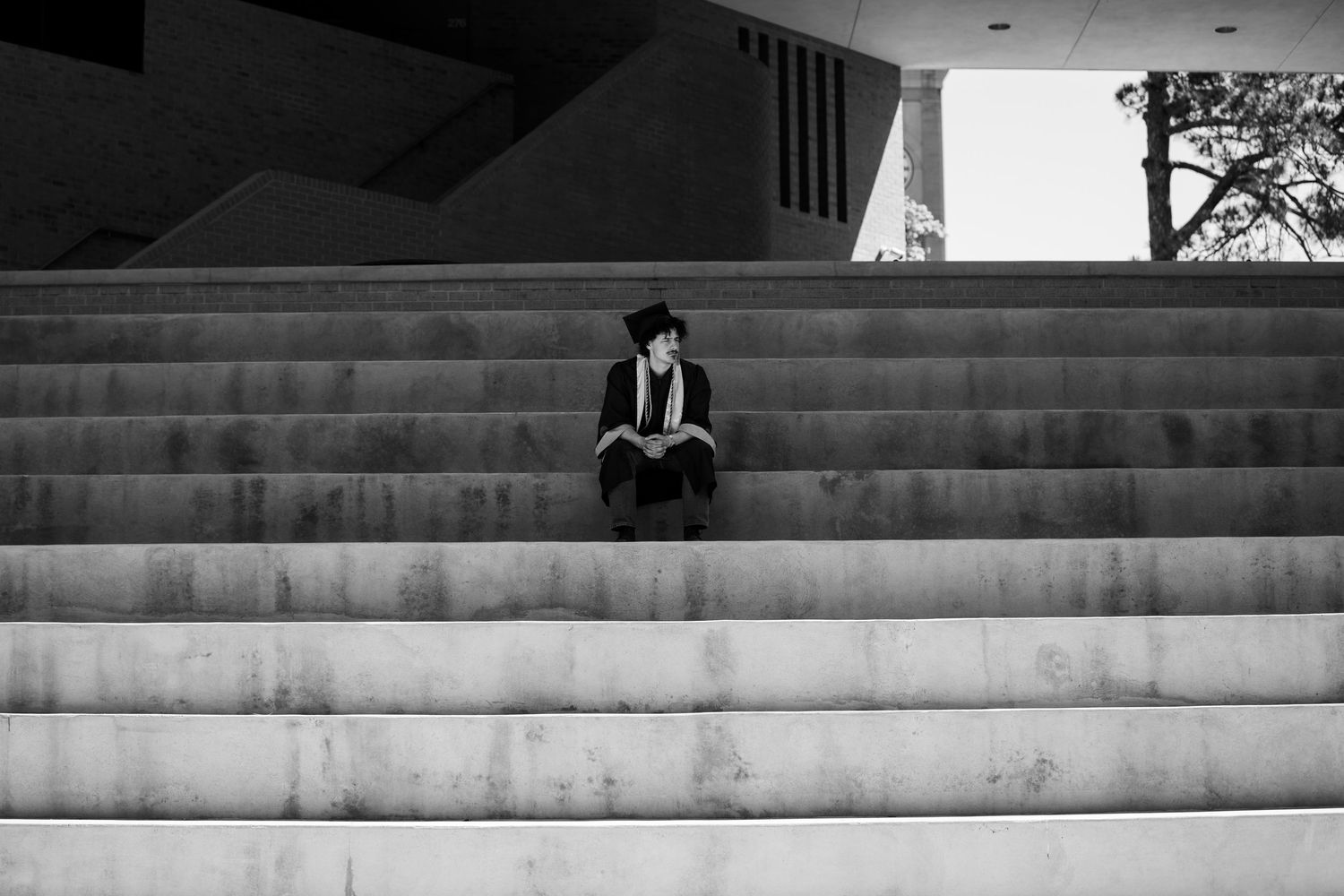 Person in hat sitting alone on wide concrete steps in a black and white urban architectural photo.