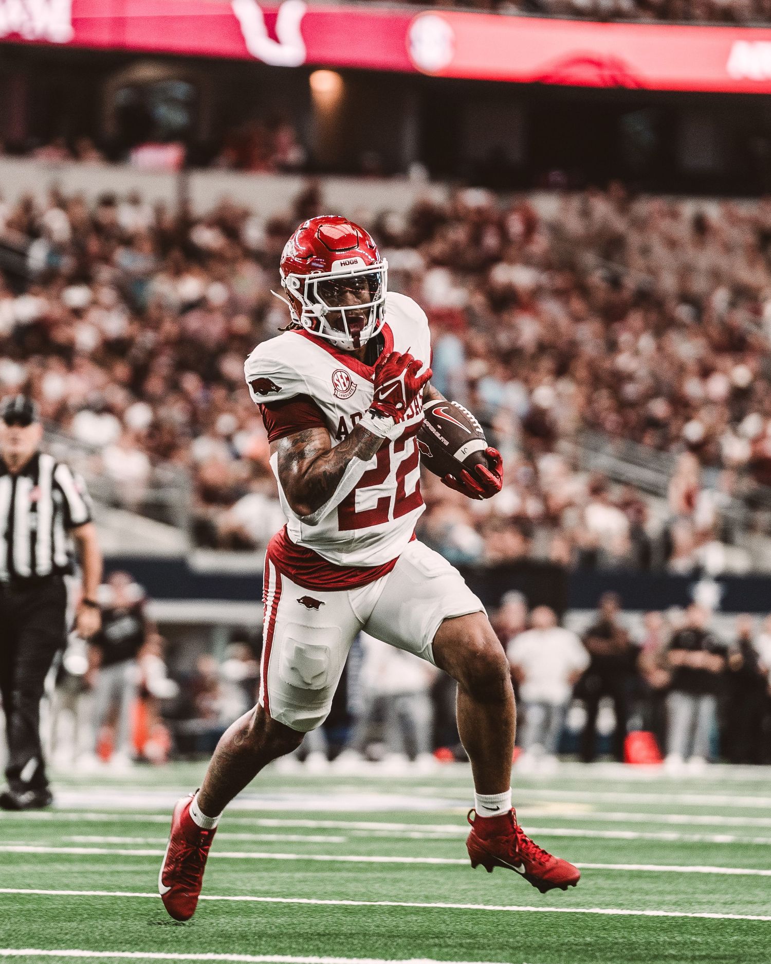 Arkansas Razorbacks football player in white jersey number 22 carries the ball during game action in a stadium.