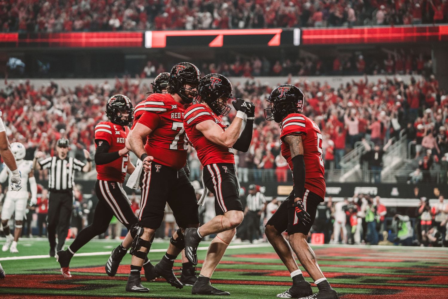Red football team players celebrate a touchdown together on the field during an exciting college football game.