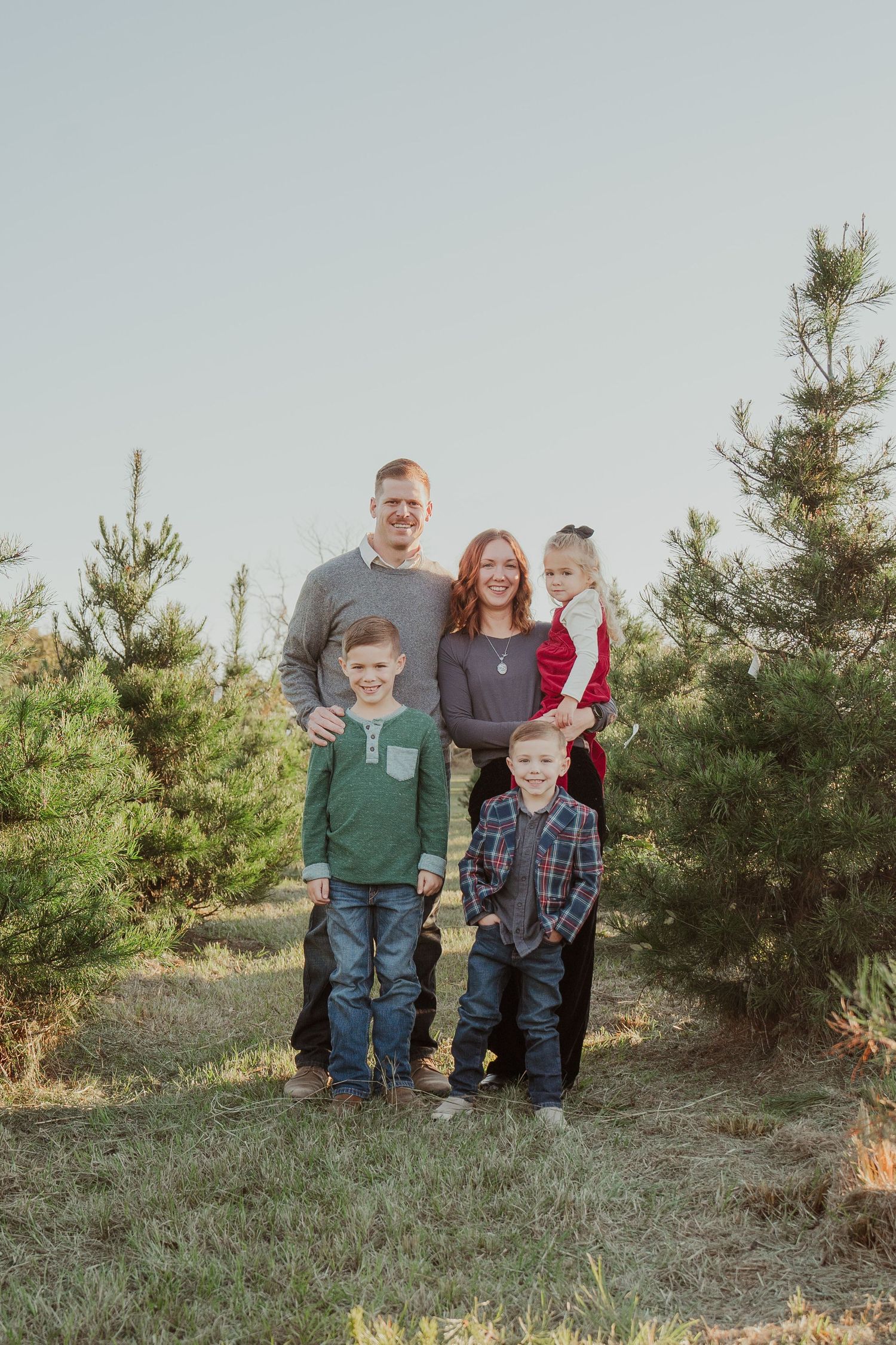 Family poses together among evergreen trees during outdoor photo session.
