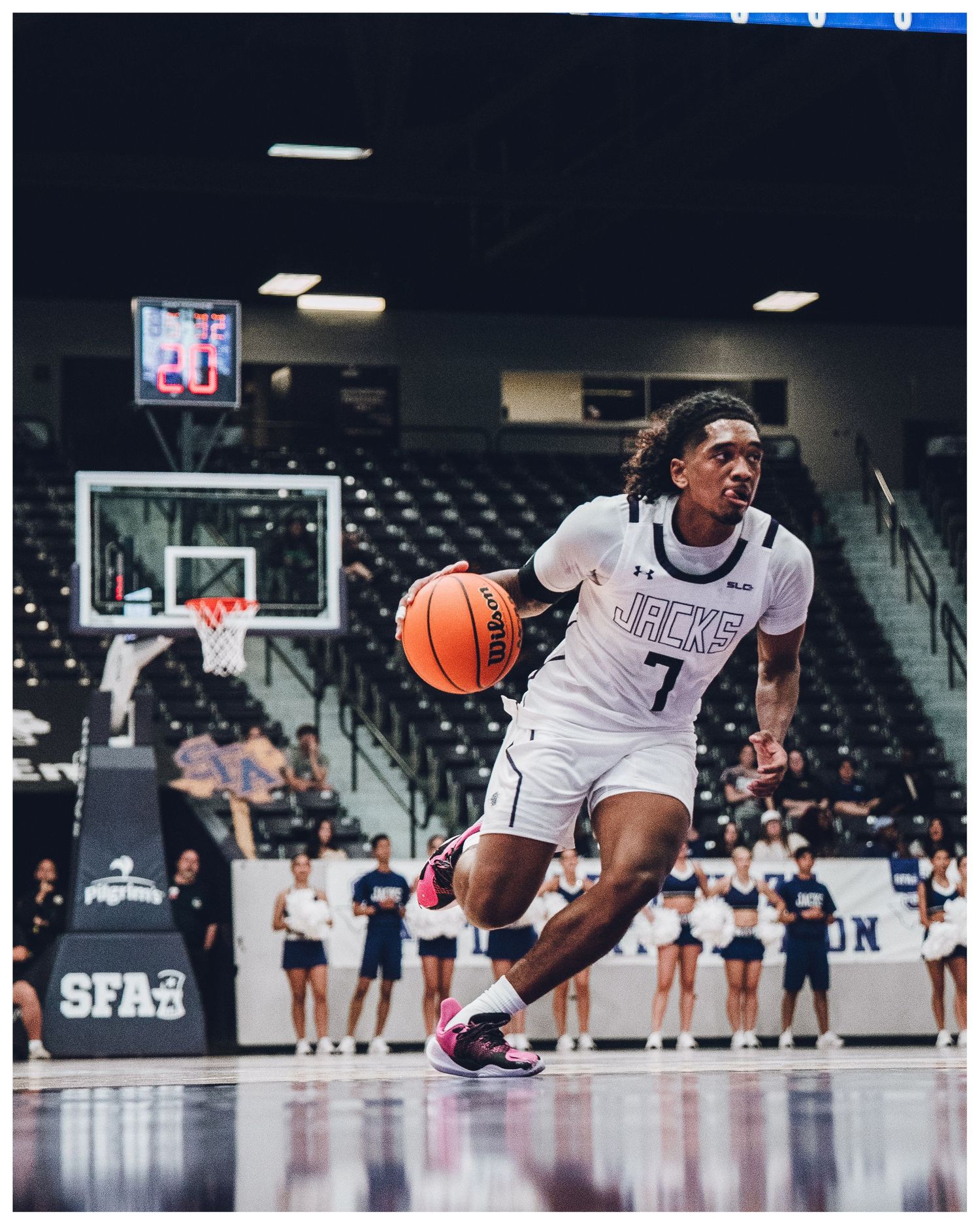 Basketball player in white jersey leaps through the air while dribbling on indoor court during competitive game.
