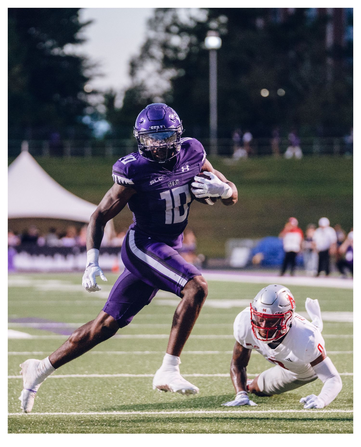 Purple-uniformed football player #10 evades a red-jersied defender during a college football game on a purple turf field.