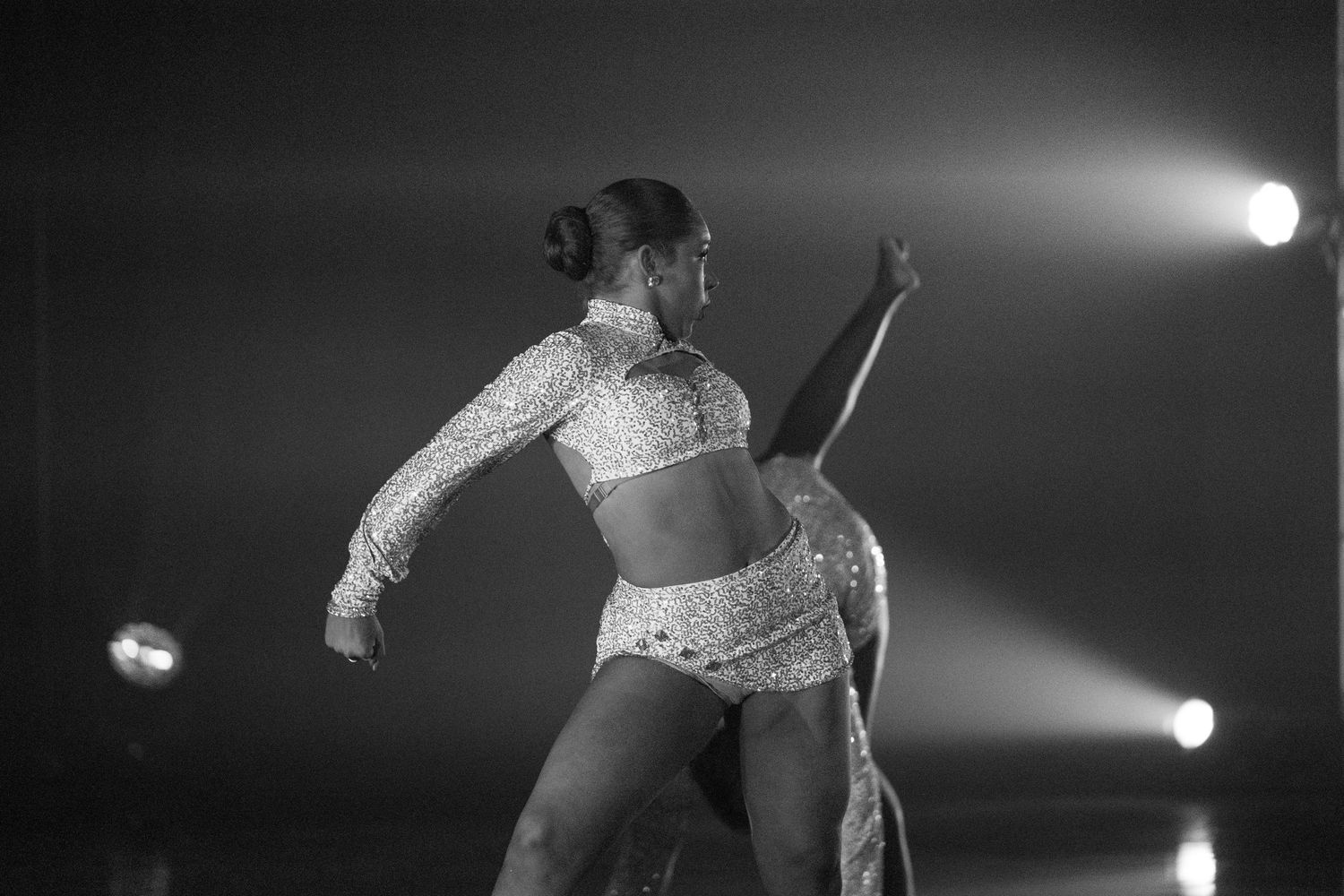 Stage performance with spotlights illuminating dancers in sequined costumes creating dramatic silhouettes.