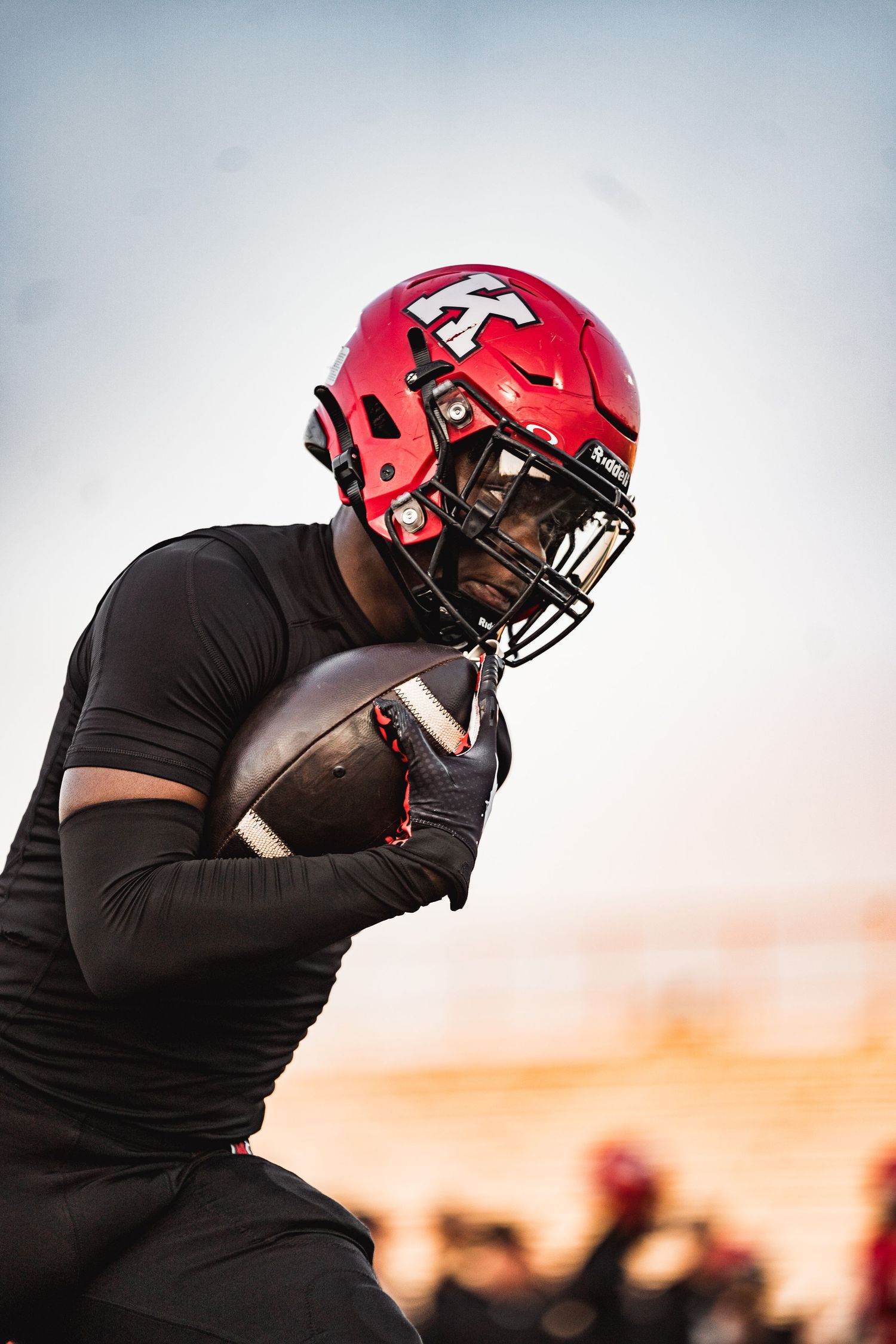 Football player in red helmet silhouetted against sunset sky during practice.