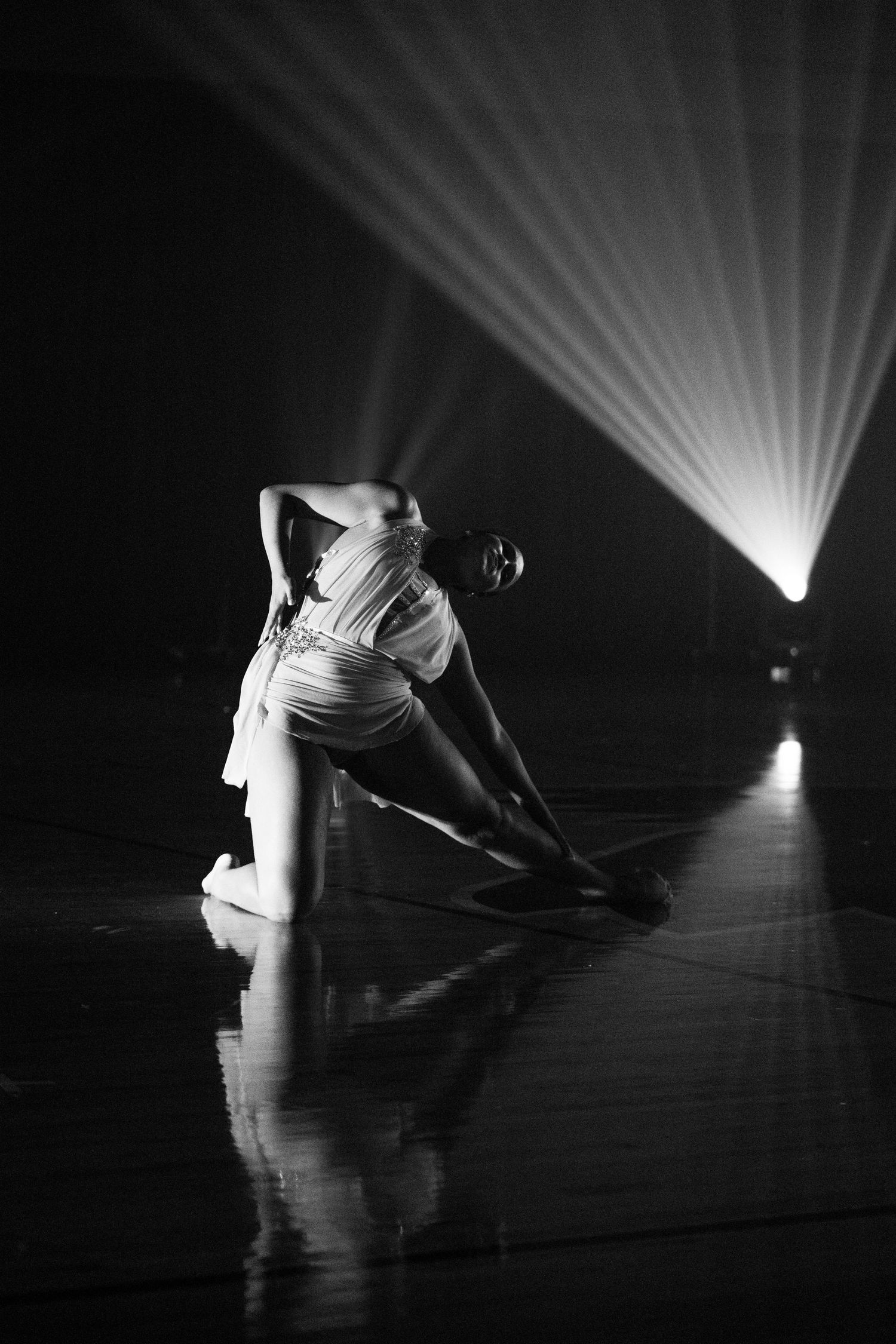 Dramatic black and white photo of a dancer in a floor pose illuminated by a bright spotlight.