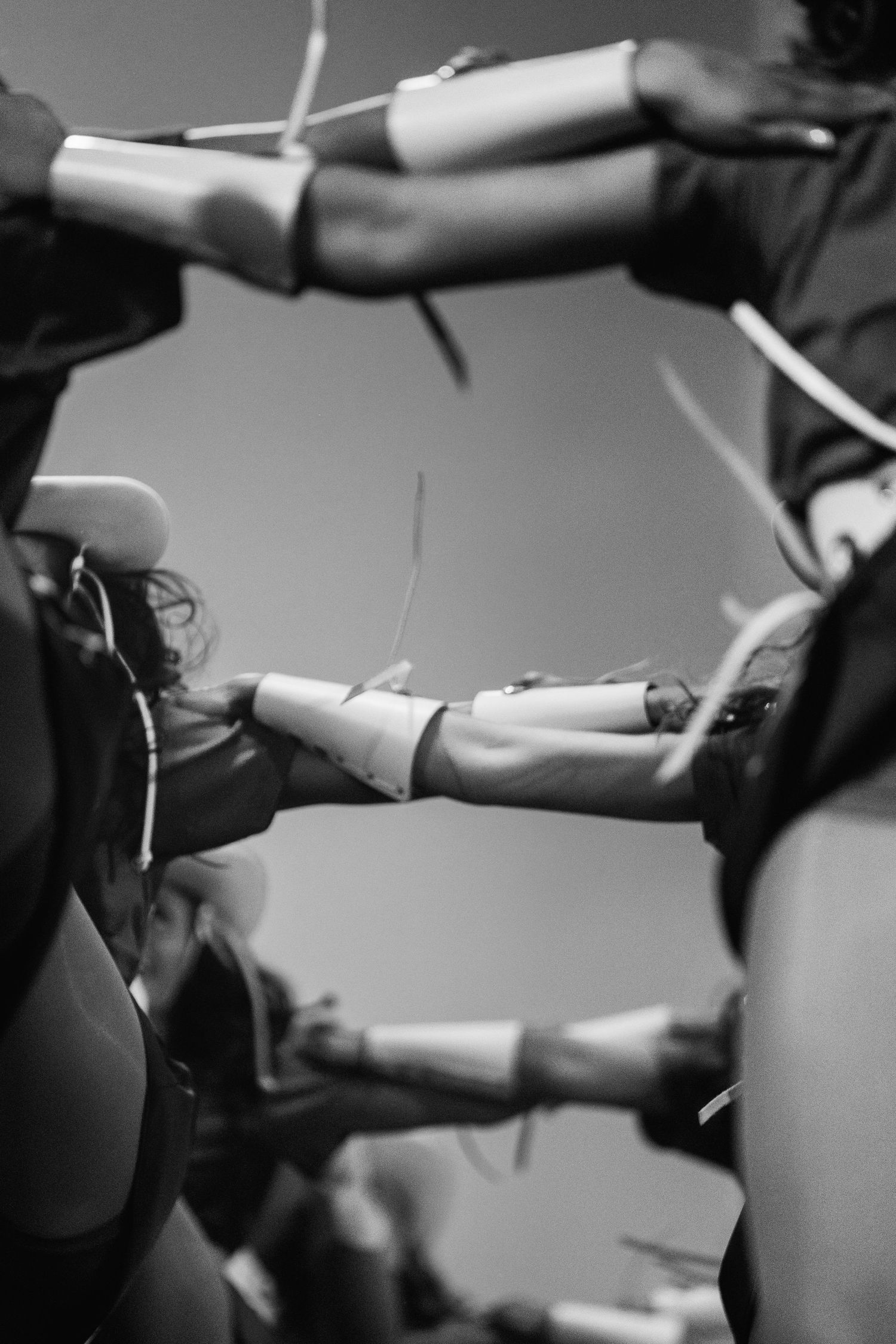 Black and white photo of performers holding batons in a circle, arms extended inward during a rhythmic group routine.