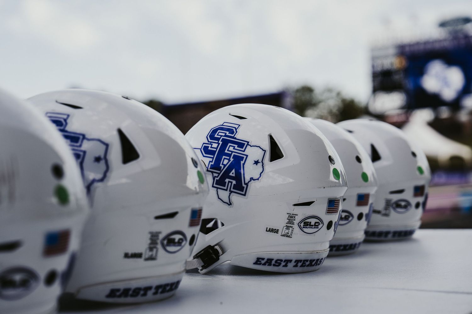 Row of white football helmets lined up on display showing team logos and protective gear.