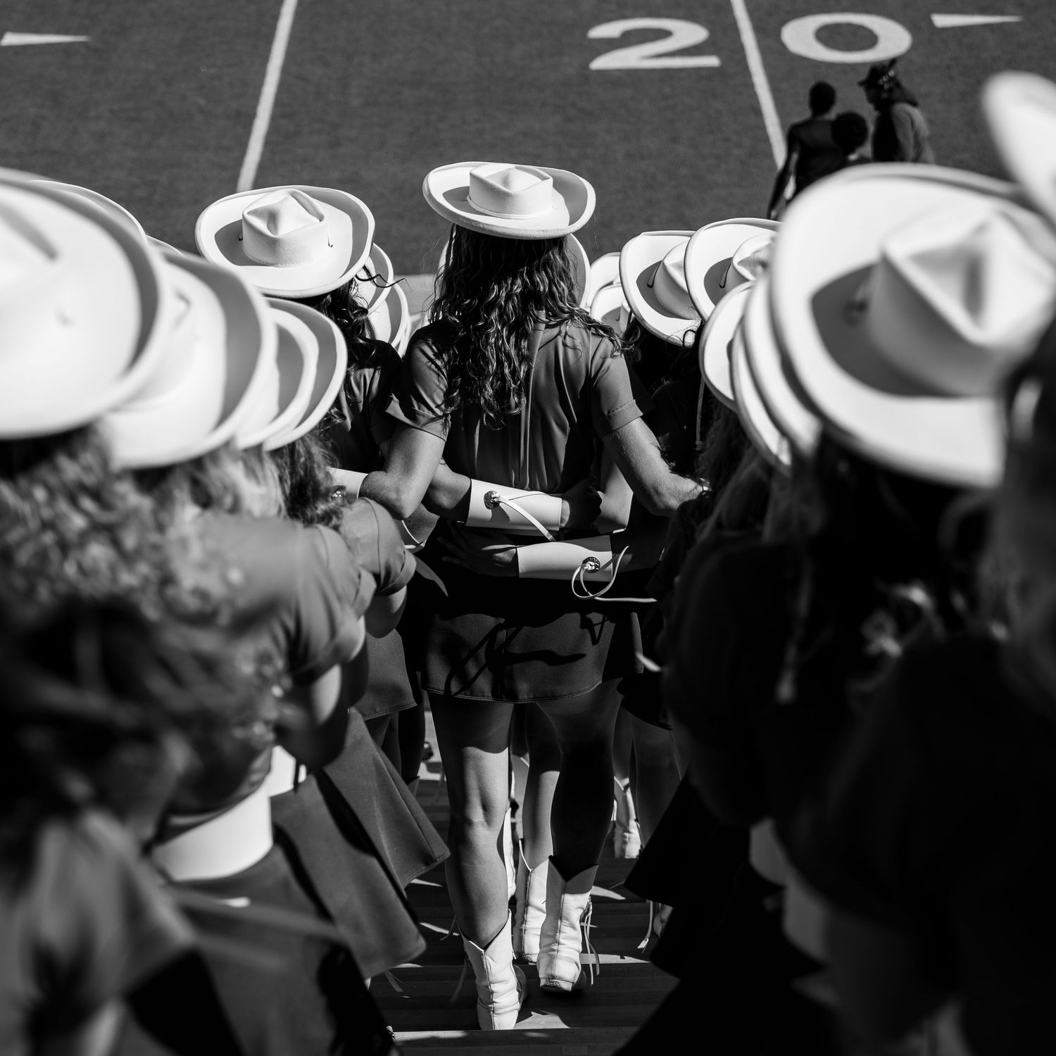 Monochrome shot of a crowd wearing white western hats viewed from behind at an outdoor gathering.