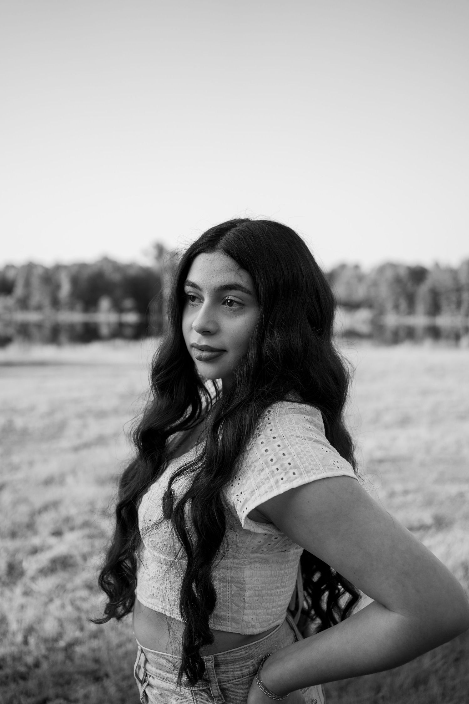 Black and white portrait of a woman with long wavy hair in an outdoor setting with trees in background.