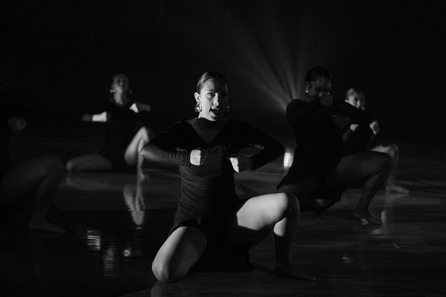 Modern dancers perform a synchronized floor routine in dramatic stage lighting.