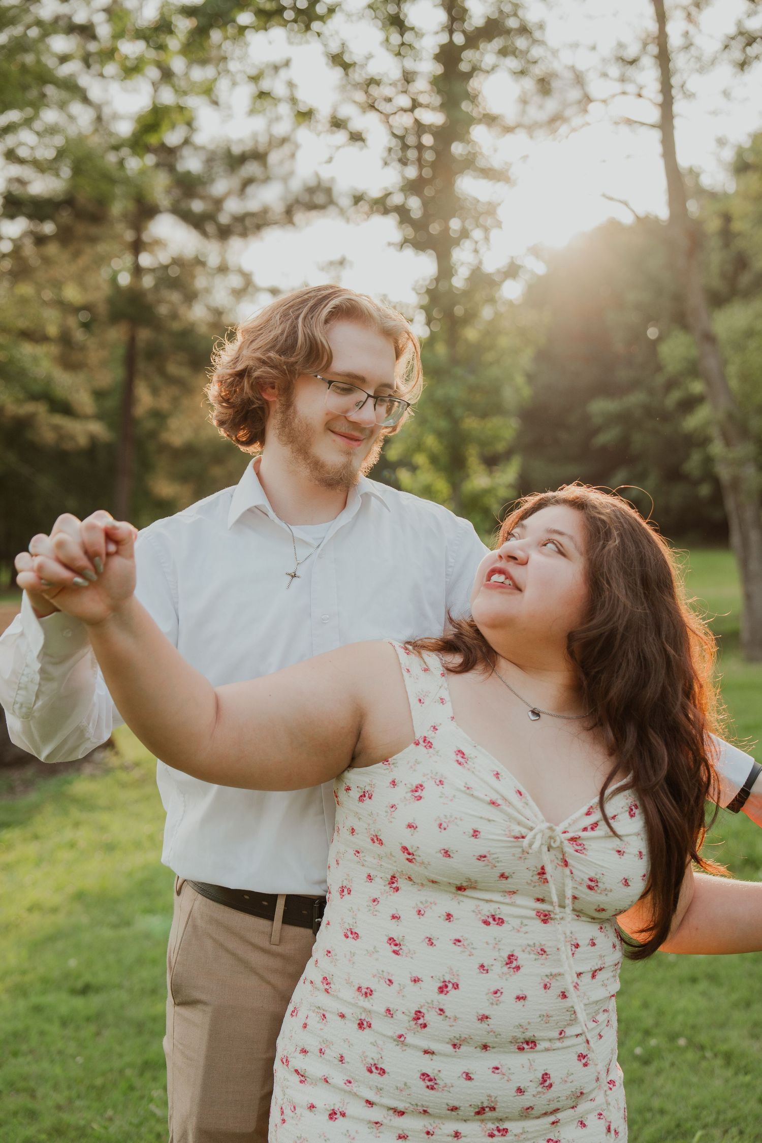 A romantic couple dances together in a sunlit garden setting wearing casual summer attire.