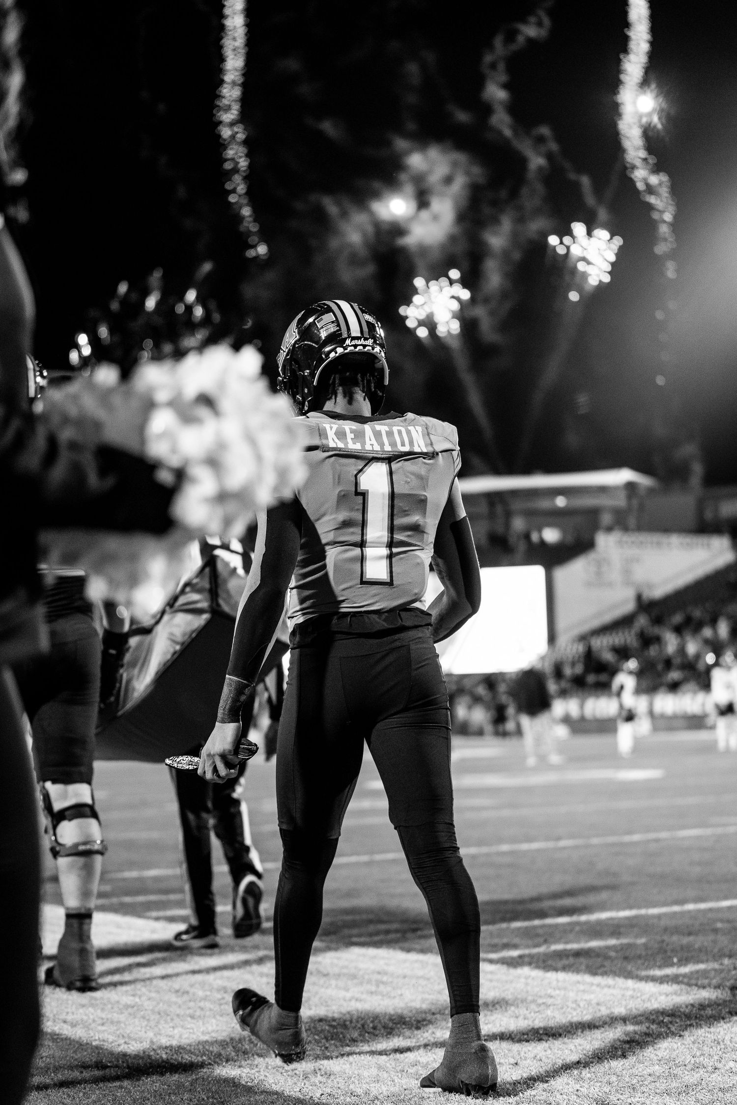 Black and white photo of football player Keaton wearing jersey number 1, standing on field with fireworks in background at night.