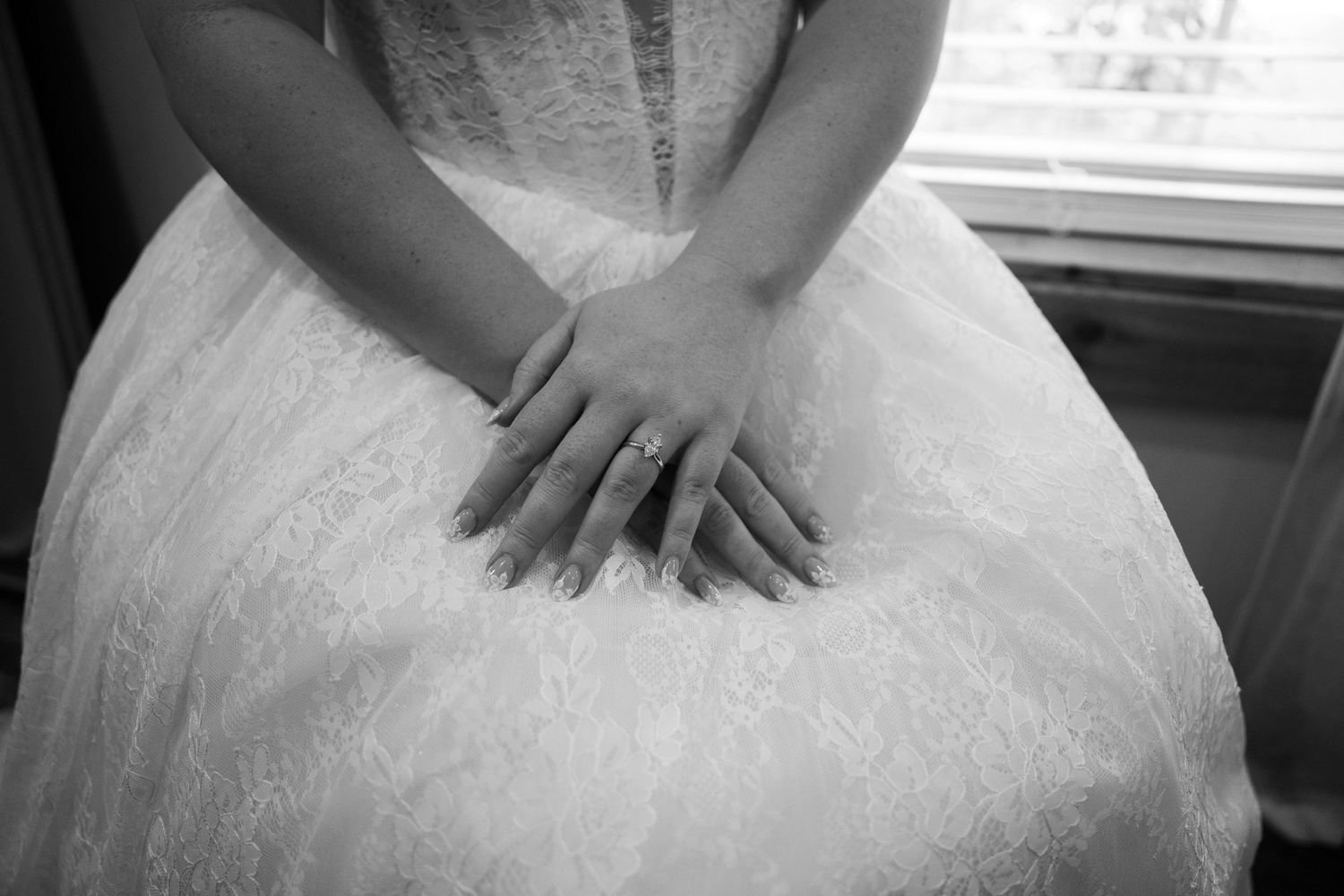 Black and white photo of a bride in lace wedding dress showing her engagement ring on folded hands.