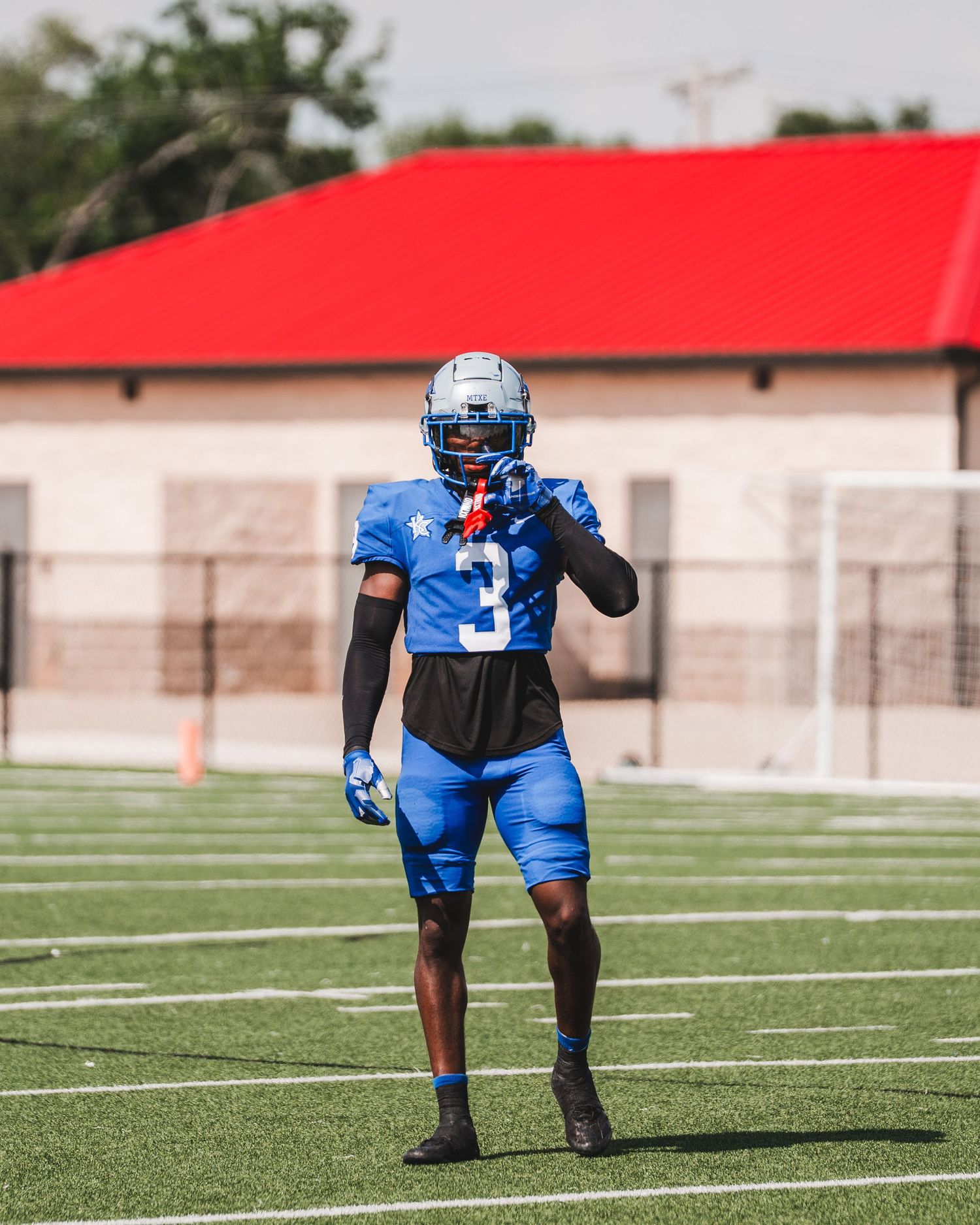 Football player stands ready on field wearing blue uniform with helmet and cleats.