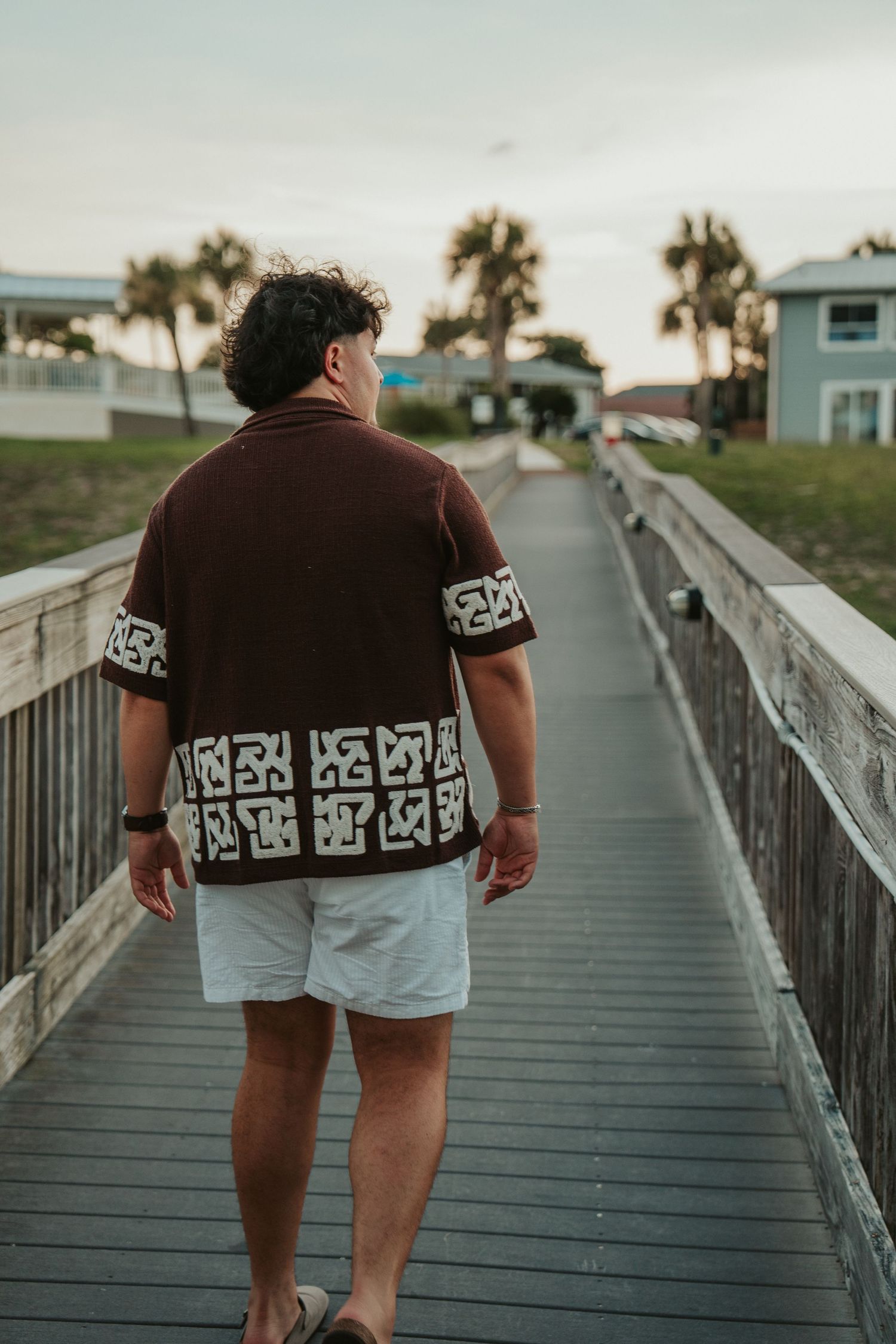 Person walking on wooden boardwalk wearing brown patterned shirt and white shorts.