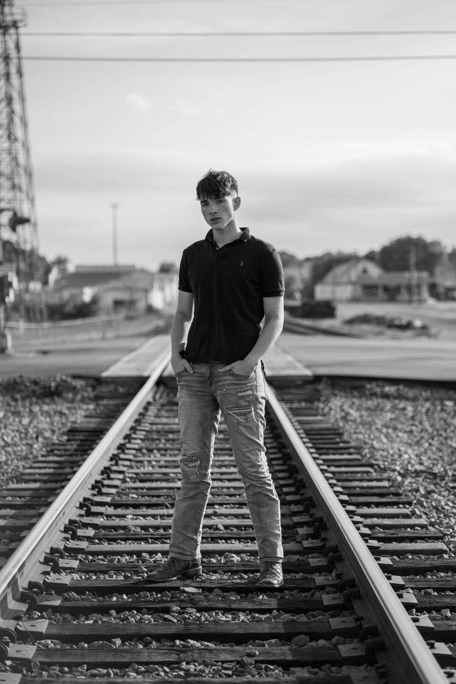 Black and white photo of person standing on train tracks in casual attire.