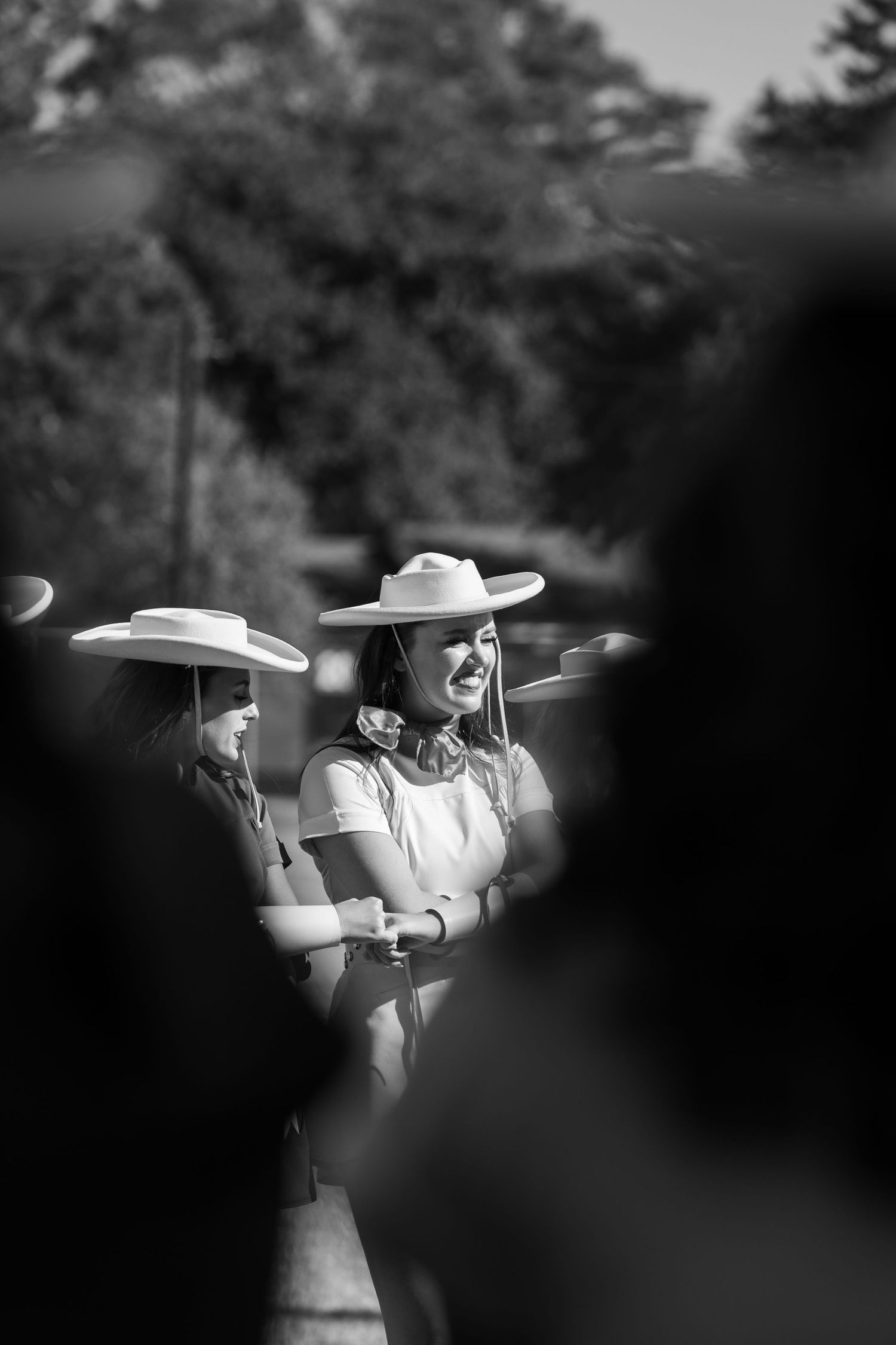 A black and white artistic photograph of people in white dresses and sun hats standing together outdoors.