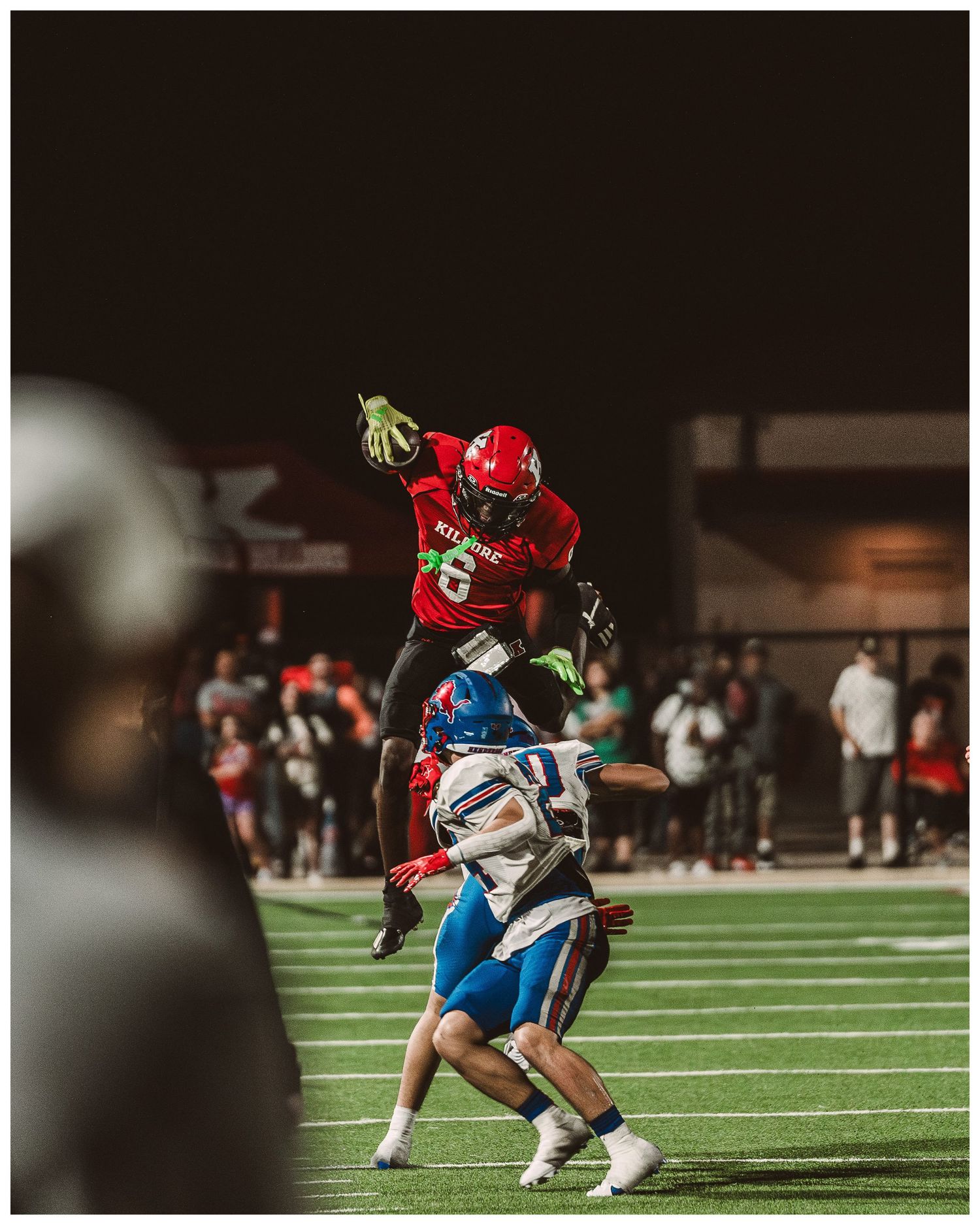 Football players engage in intense gameplay on an indoor turf field at night.
