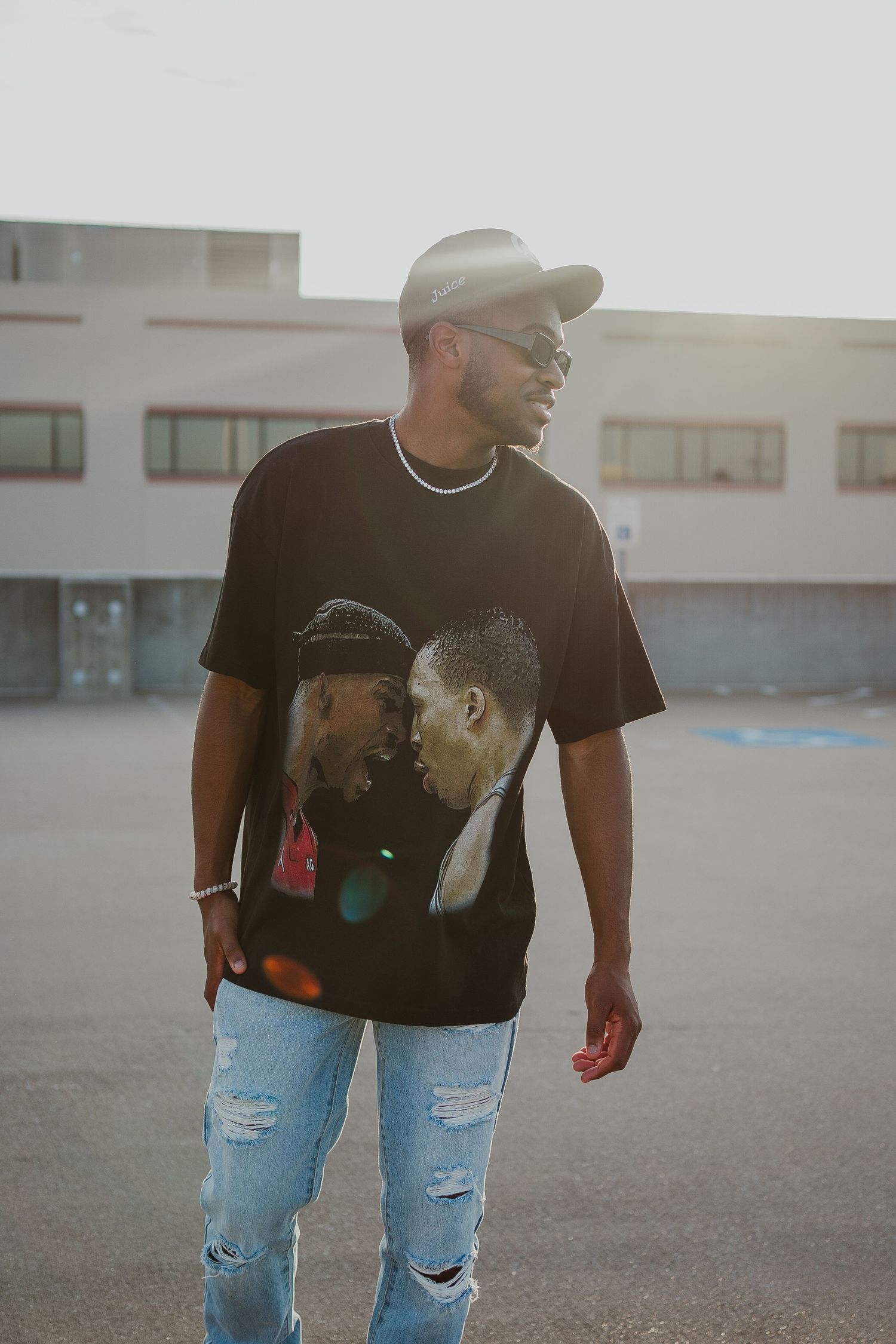 Person wearing graphic t-shirt, baseball cap and ripped jeans stands in urban setting.