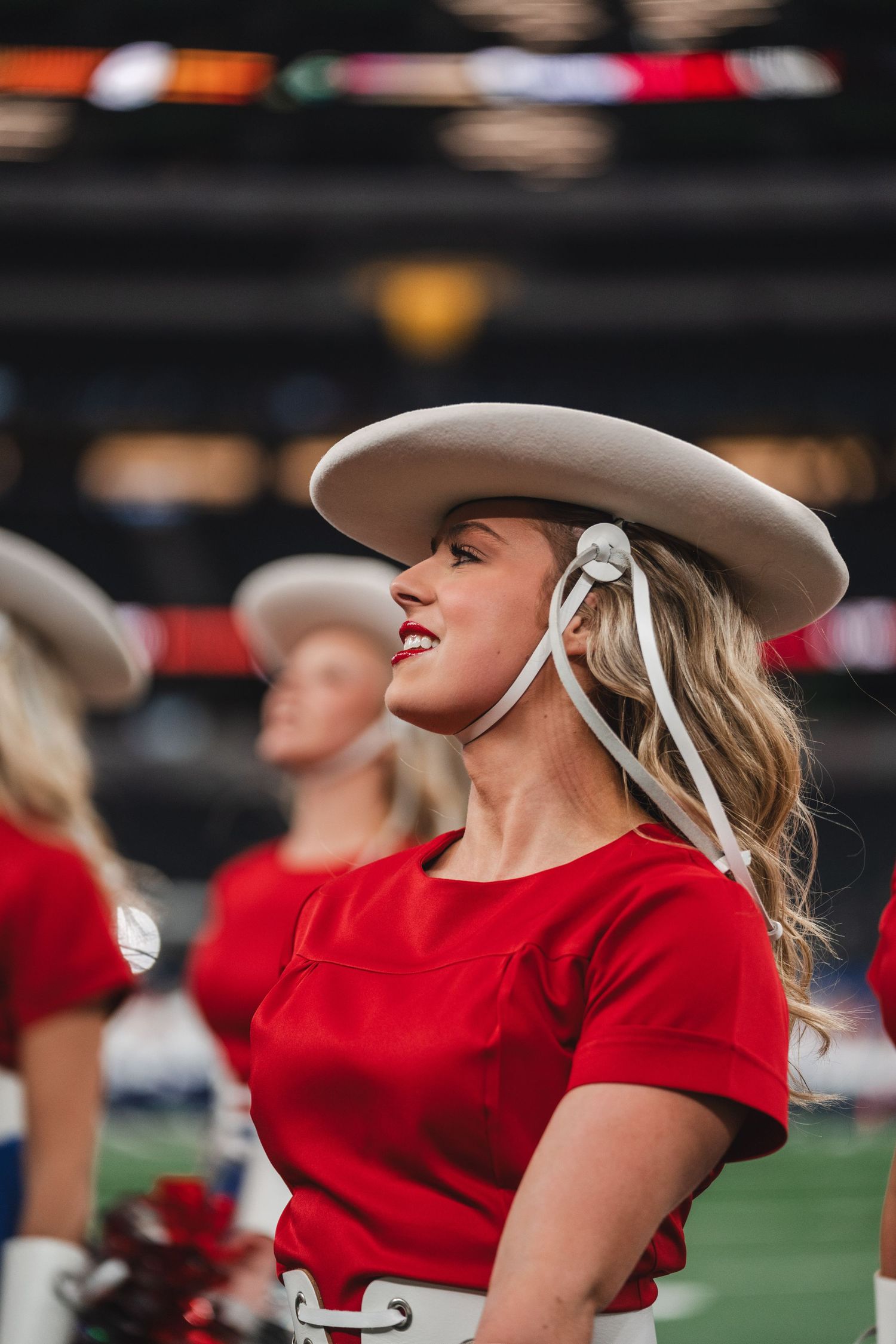 Performer in red top and white cowboy hat at stadium performance during sporting event.