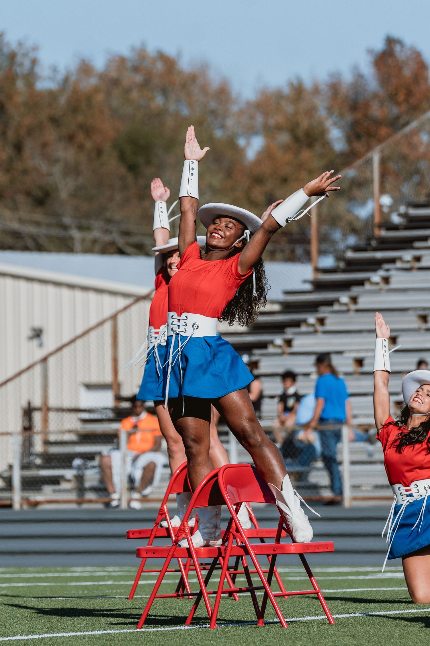 Cheerleader performing on red chairs during outdoor stadium performance in red and blue uniform.