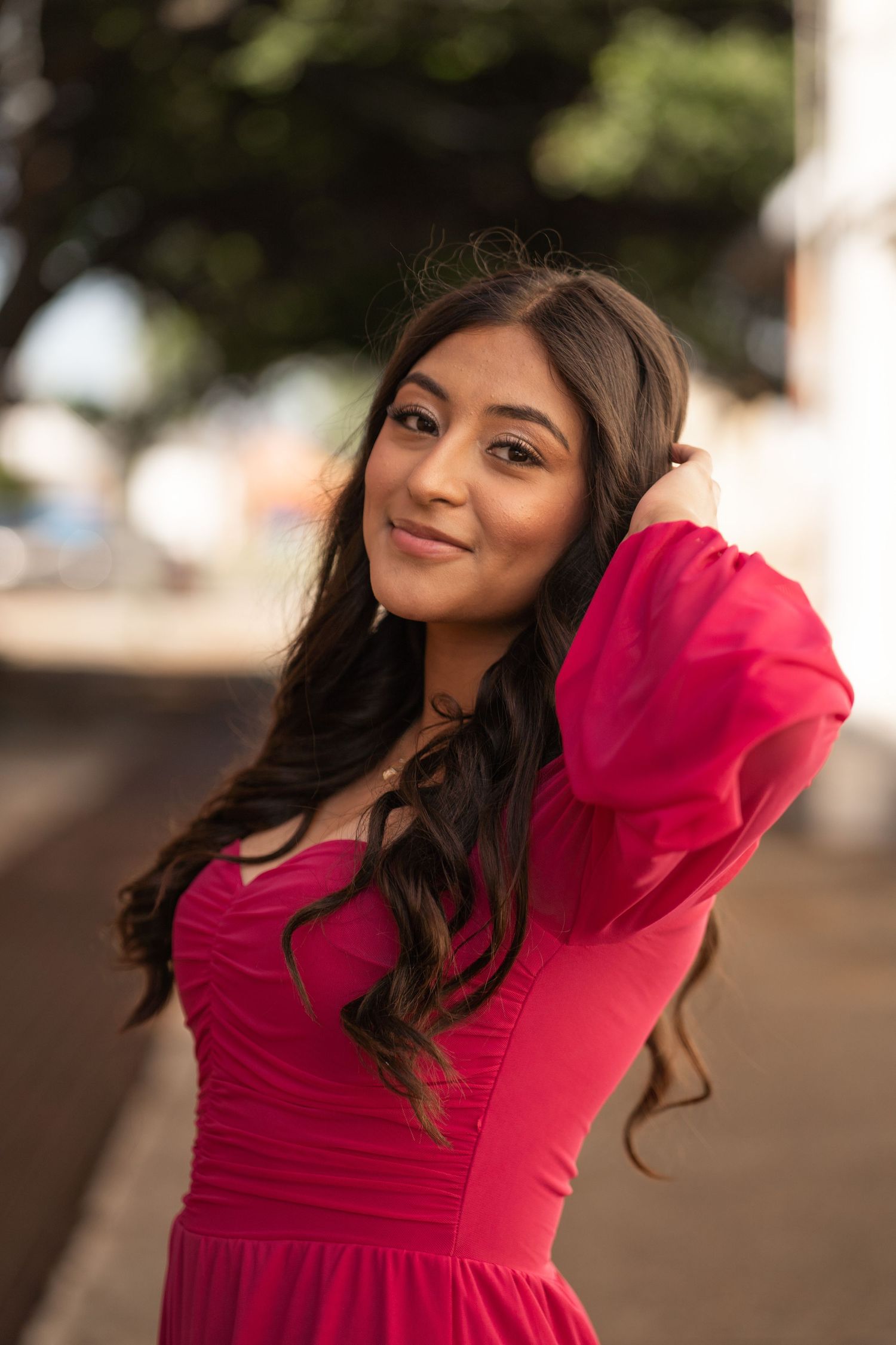 Portrait of someone in vibrant red formal dress with long dark hair outdoors.