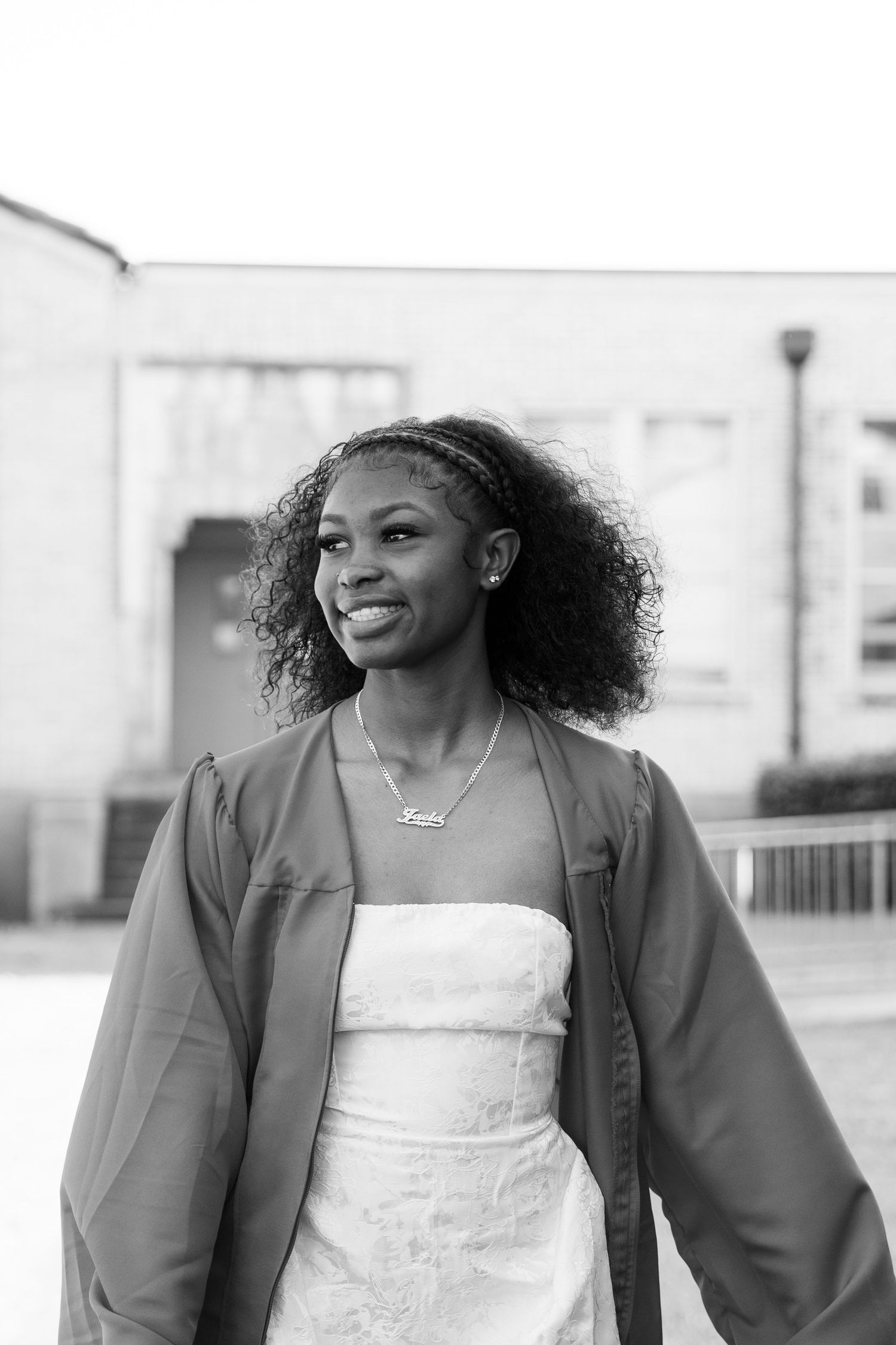 A woman in a white dress and dark jacket smiles while standing outdoors in a black and white photograph.