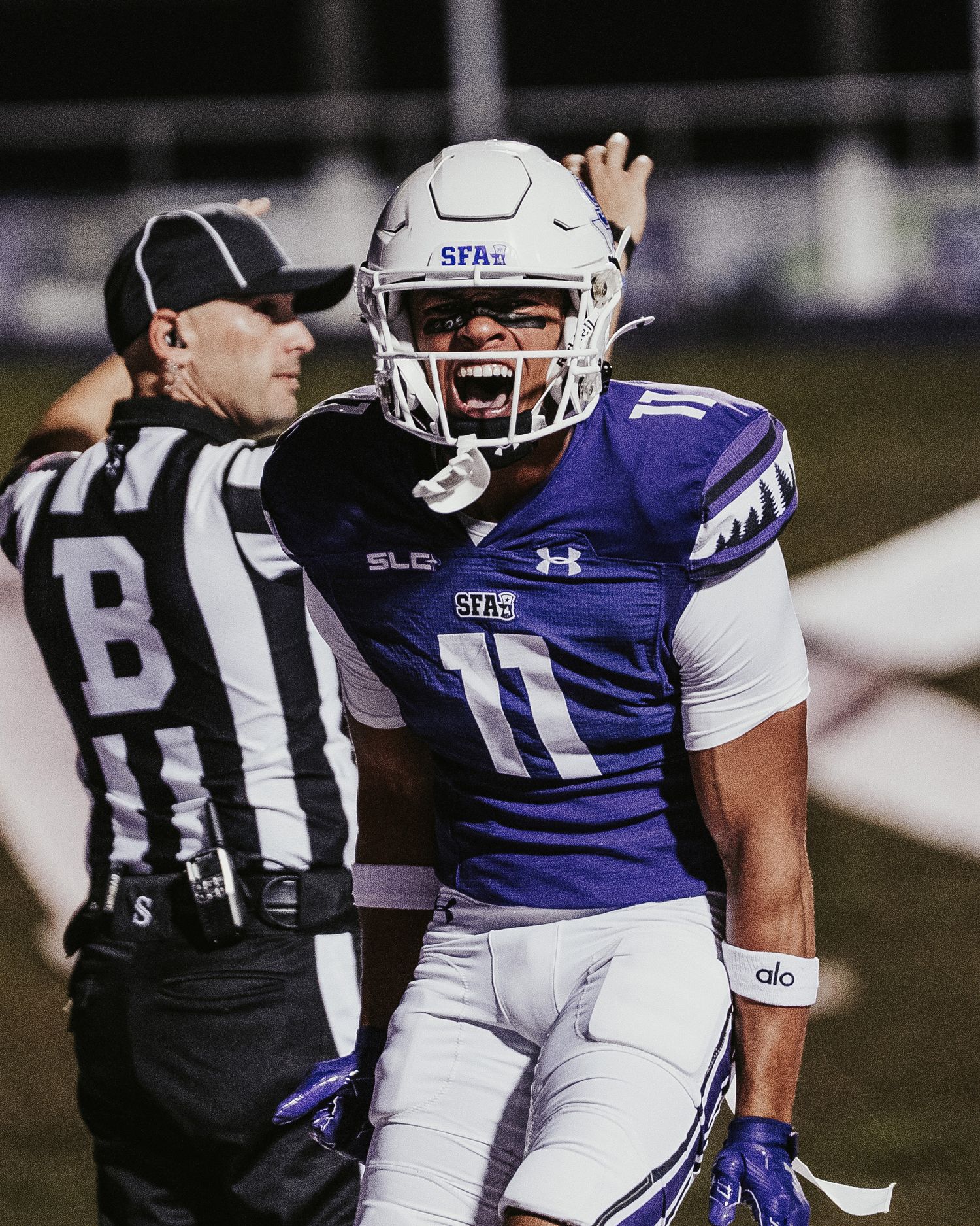 SFA Lumberjacks football player #11 celebrates on field at night game, referee visible in background.