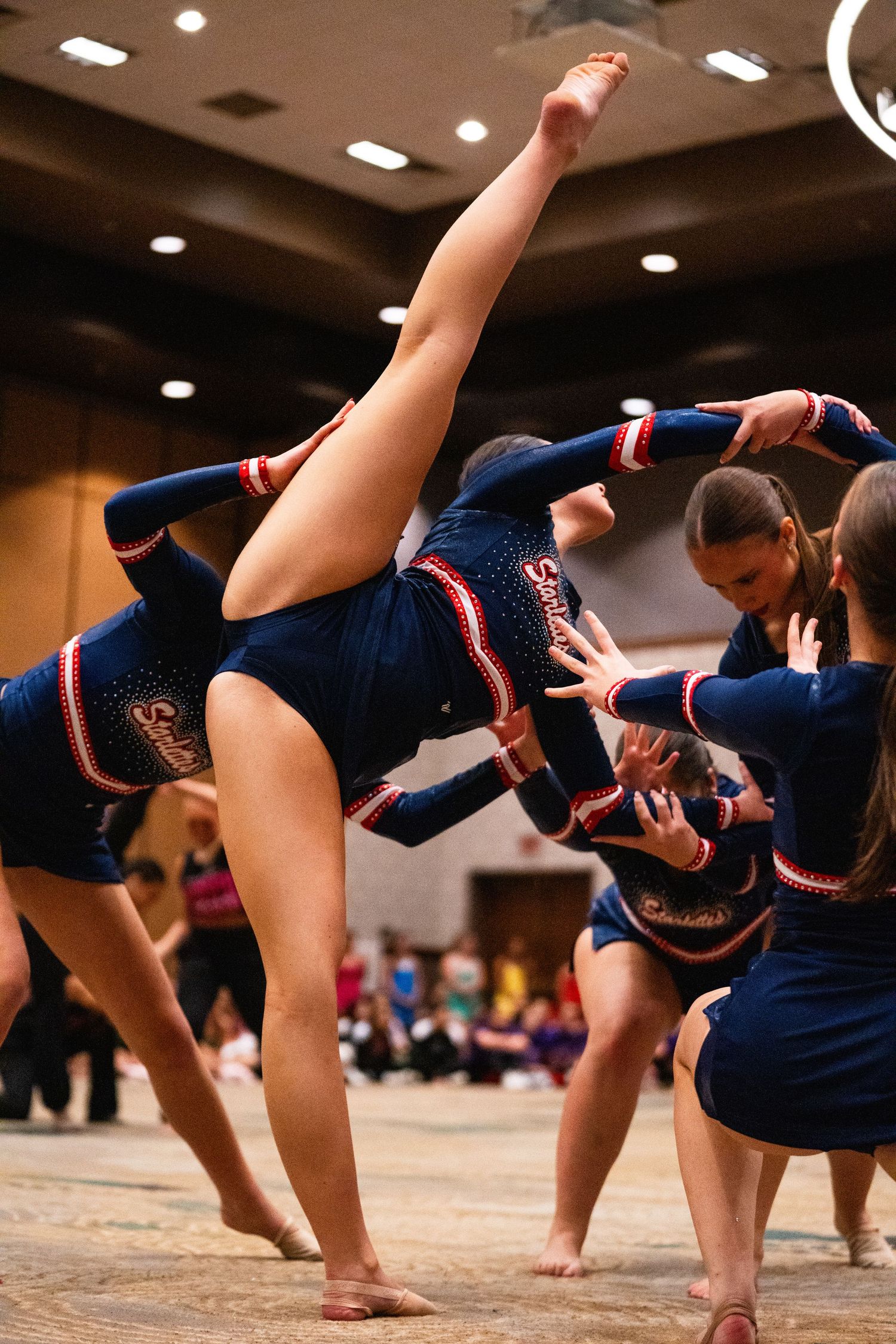 Cheerleaders in navy blue uniforms perform a stunning acrobatic routine at an indoor cheerleading competition.