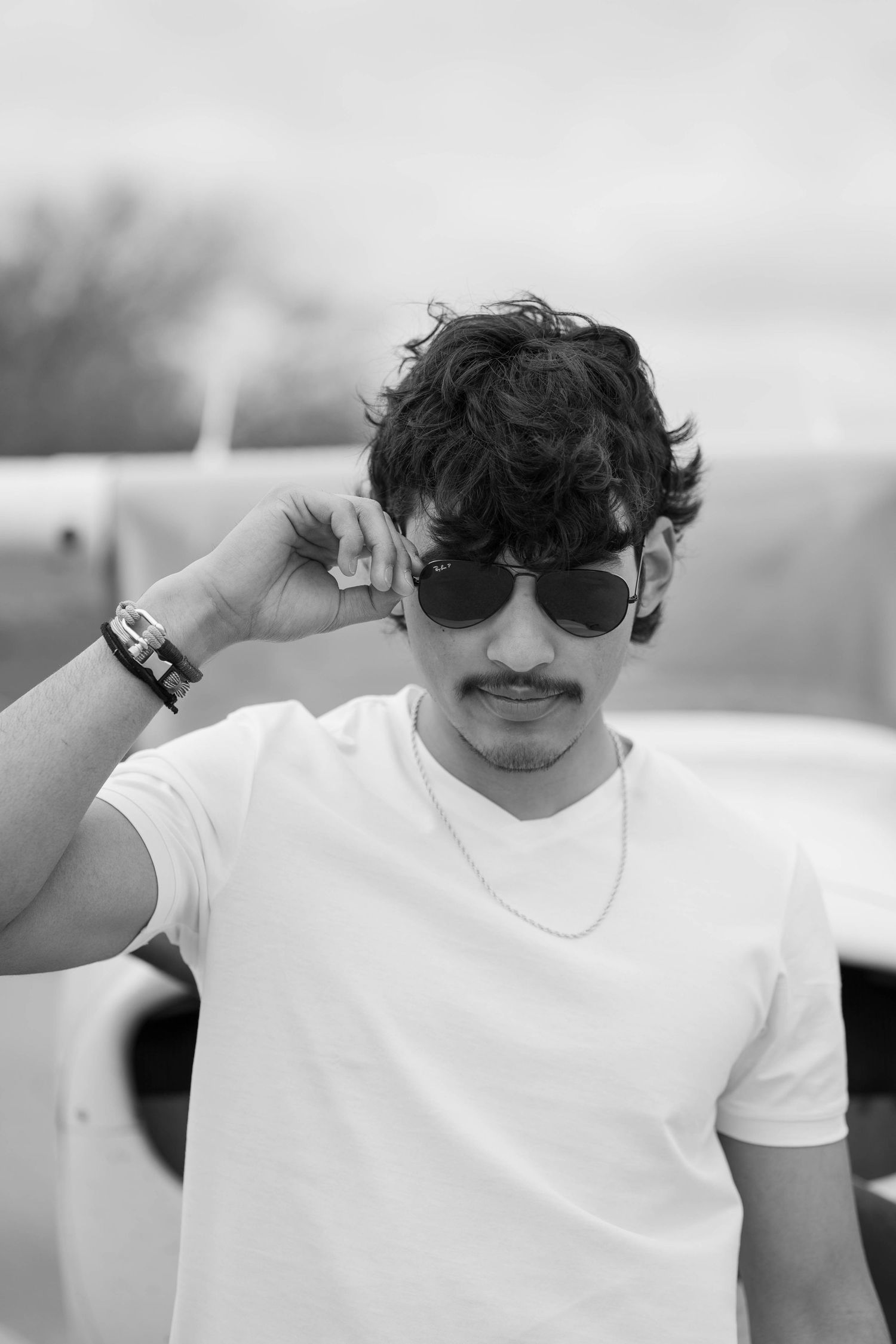 Stylish portrait of person in white t-shirt adjusting sunglasses against blurred background.