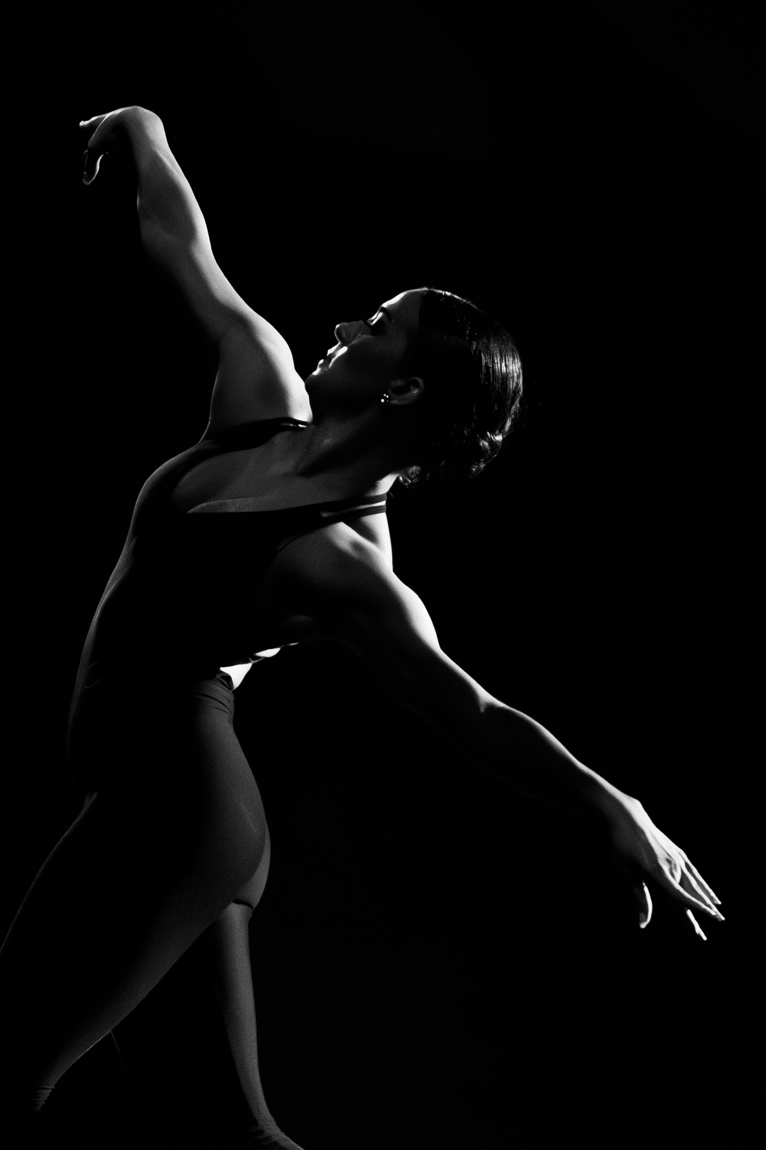 Black and white silhouette of a female dancer gracefully arching backward with arms extended against a dark background.