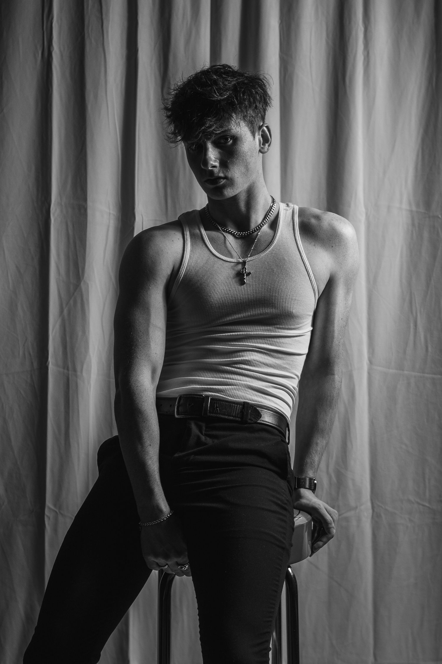 Dramatic black and white portrait of person in tank top against curtain backdrop.