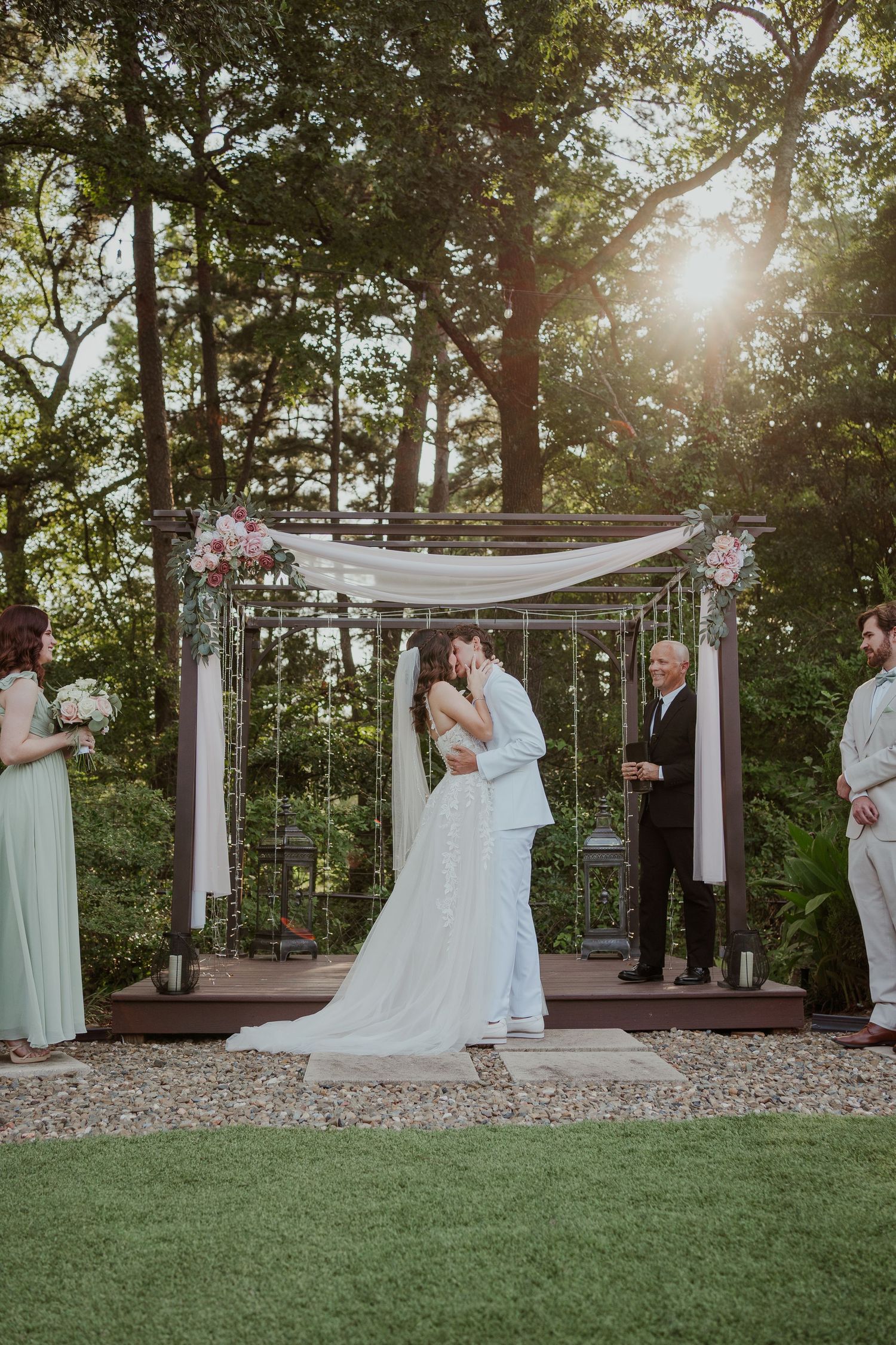 Outdoor wedding ceremony under a decorated pergola with string lights at sunset.