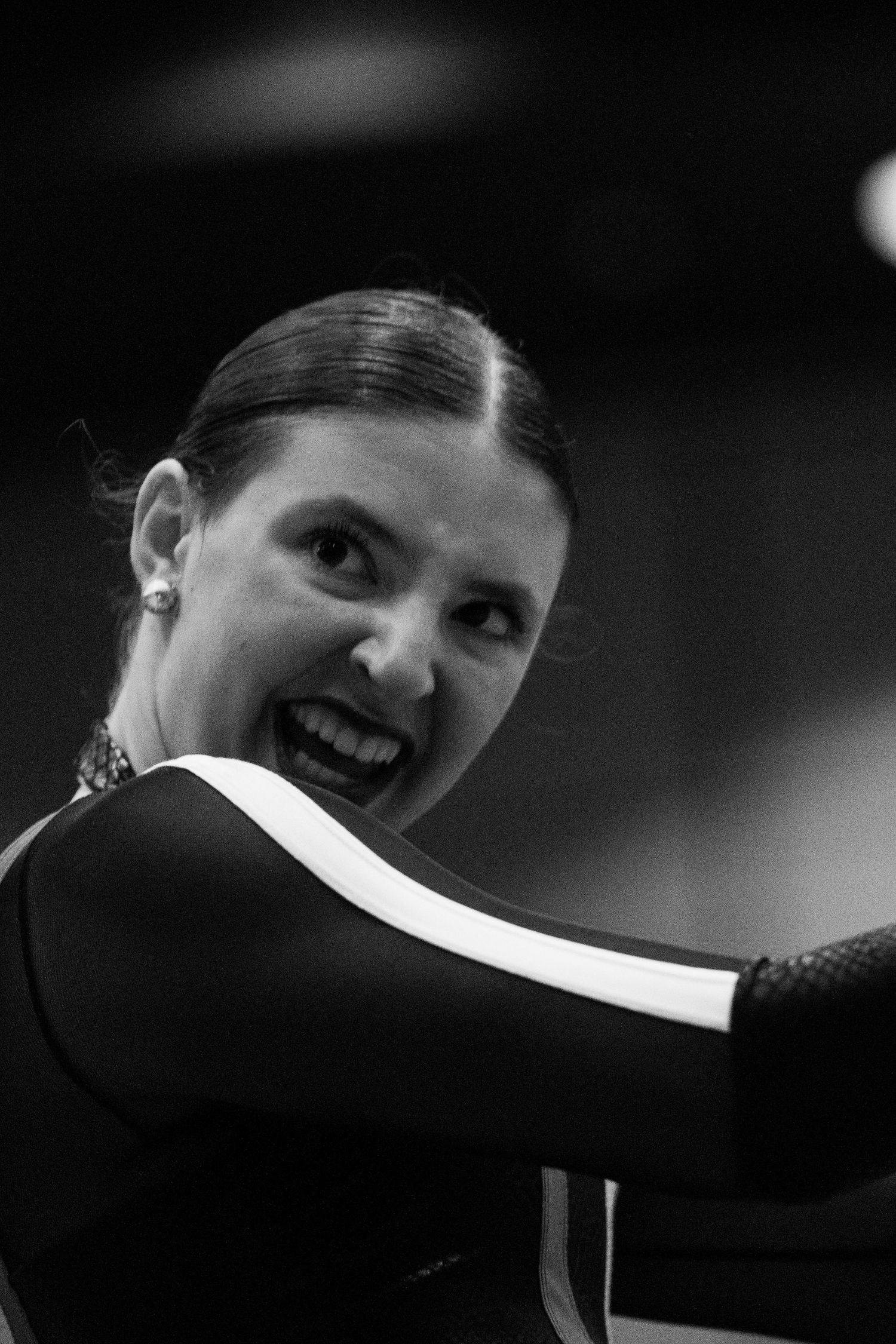Smiling woman in black and white photo wearing a dark outfit with white stripe, hair pulled back elegantly.