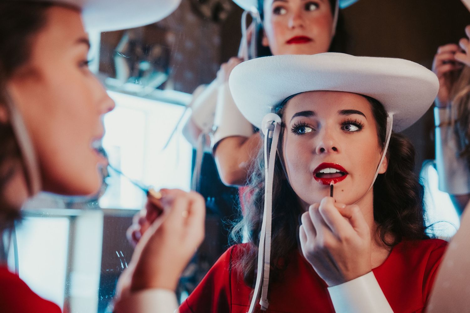 A series of photos showing someone applying red lipstick and makeup in a white cowboy hat and red top.