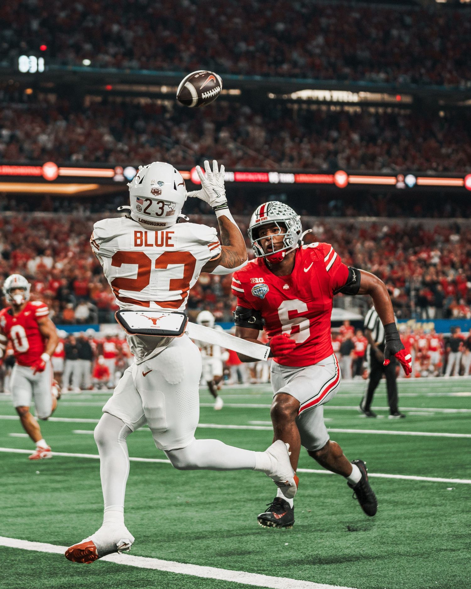 Football players compete for catch during intense game in packed stadium.