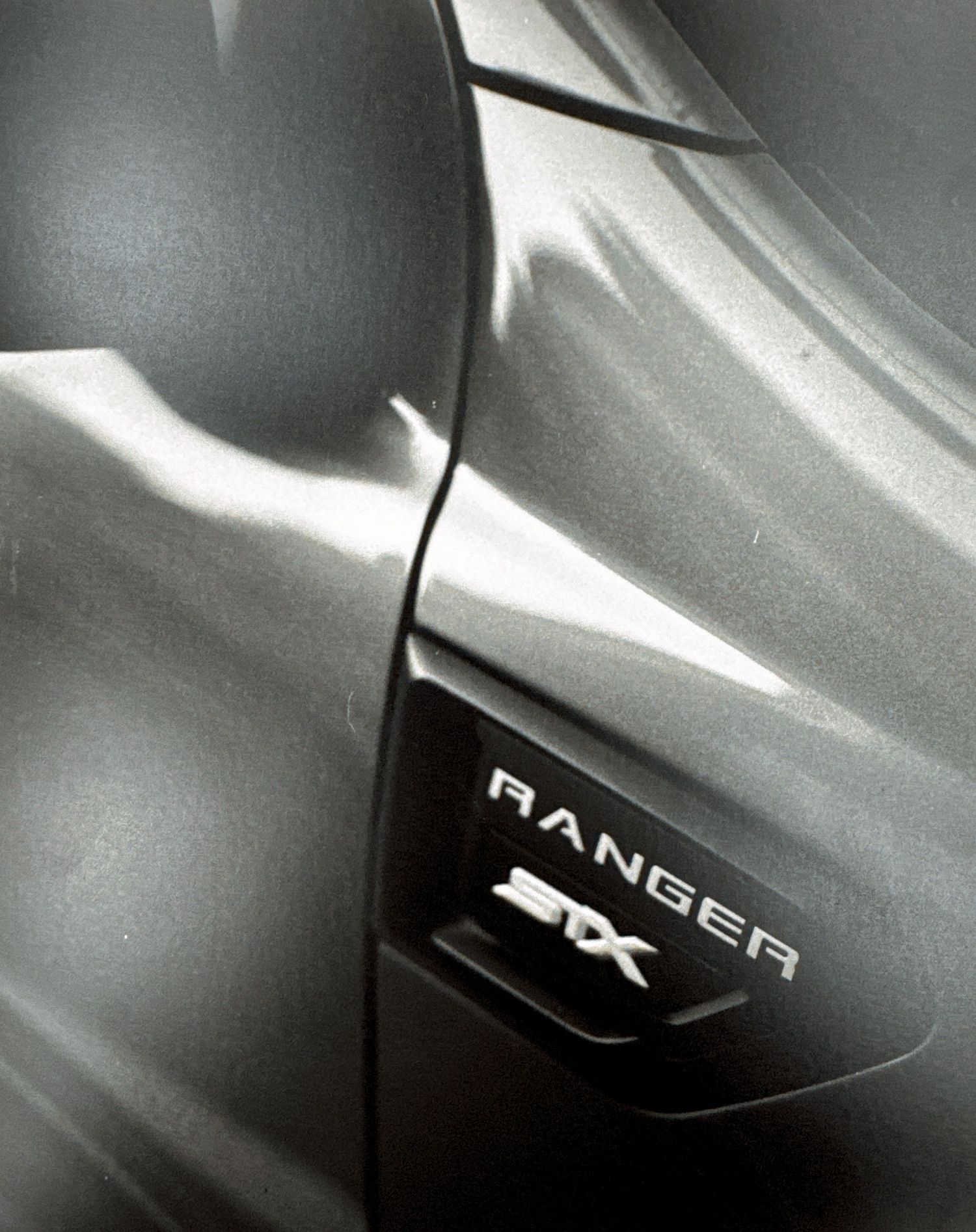 Close-up abstract view of silver metallic car body panels and badges showing sleek automotive design details.