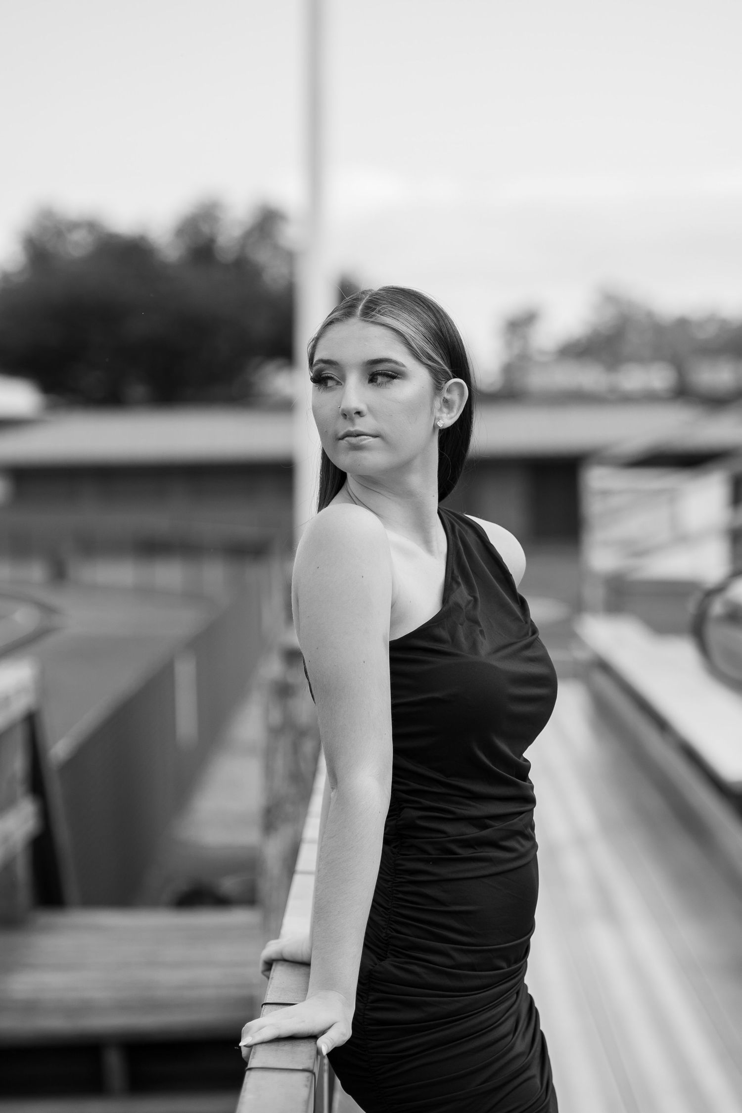 Woman in black sleeveless dress poses on urban rooftop in dramatic black and white portrait.